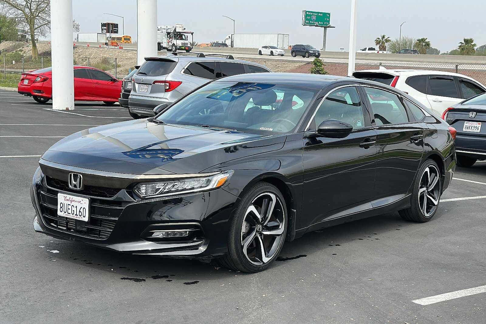 Honda Accord 桌布 壁紙 — 一架時尚黑色本田雅閣房車停泊在繁忙的瀝青停車場，背景有其他車輛和高速公路標誌。