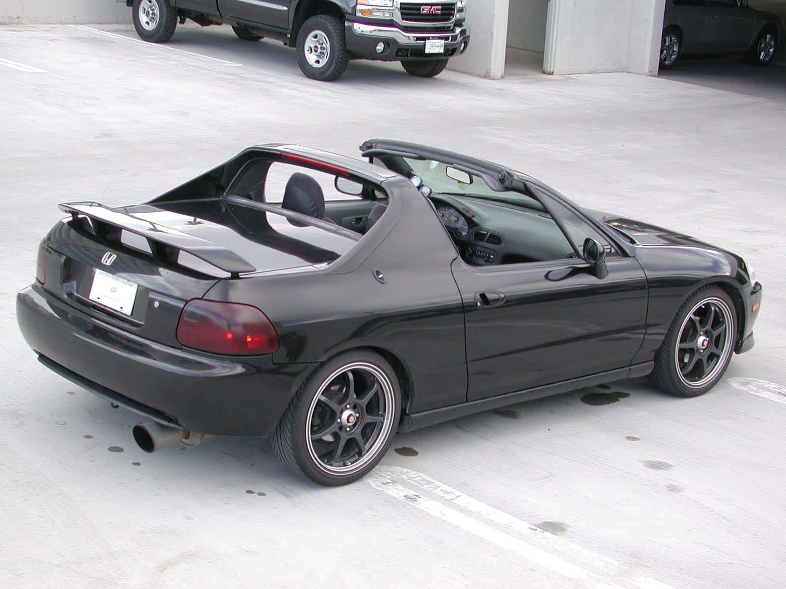 Honda Civic Del Sol 桌布 壁紙 — 一架時尚的黑色本田S2000開篷跑車停泊在混凝土停車場，背景有一輛GMC貨車。