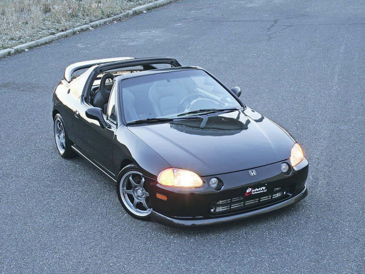 Honda Civic Del Sol 桌布 壁紙 — 一輛時尚的黑色本田S2000敞篷車，帶有發光的車頭燈，停在瀝青路上。