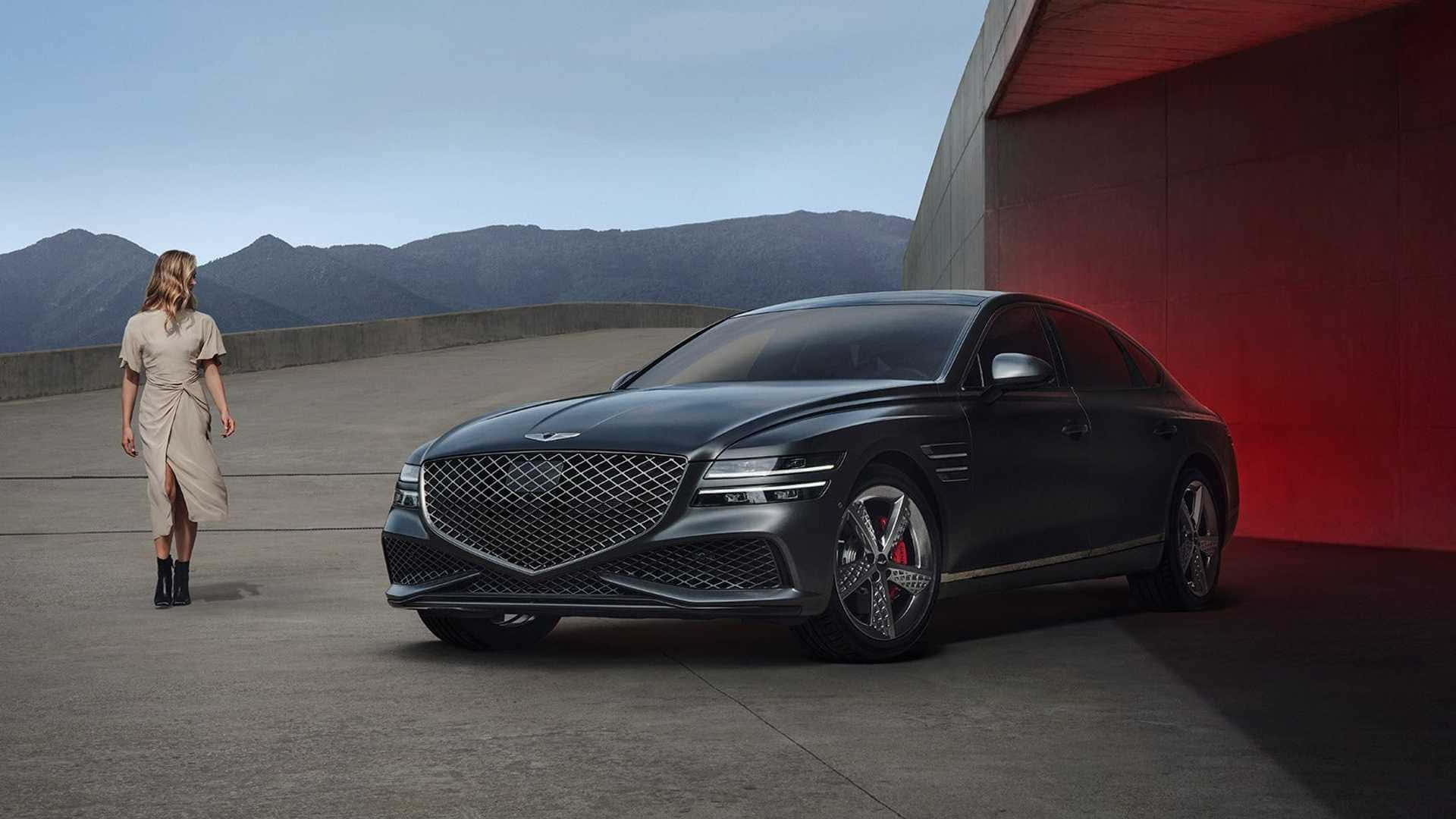 Genesis G80 桌布 壁紙 — 一輛時尚的黑色豪華轎車停泊在一位身穿米色連衣裙的女性旁邊，背景是現代紅牆和遠處的山脈。