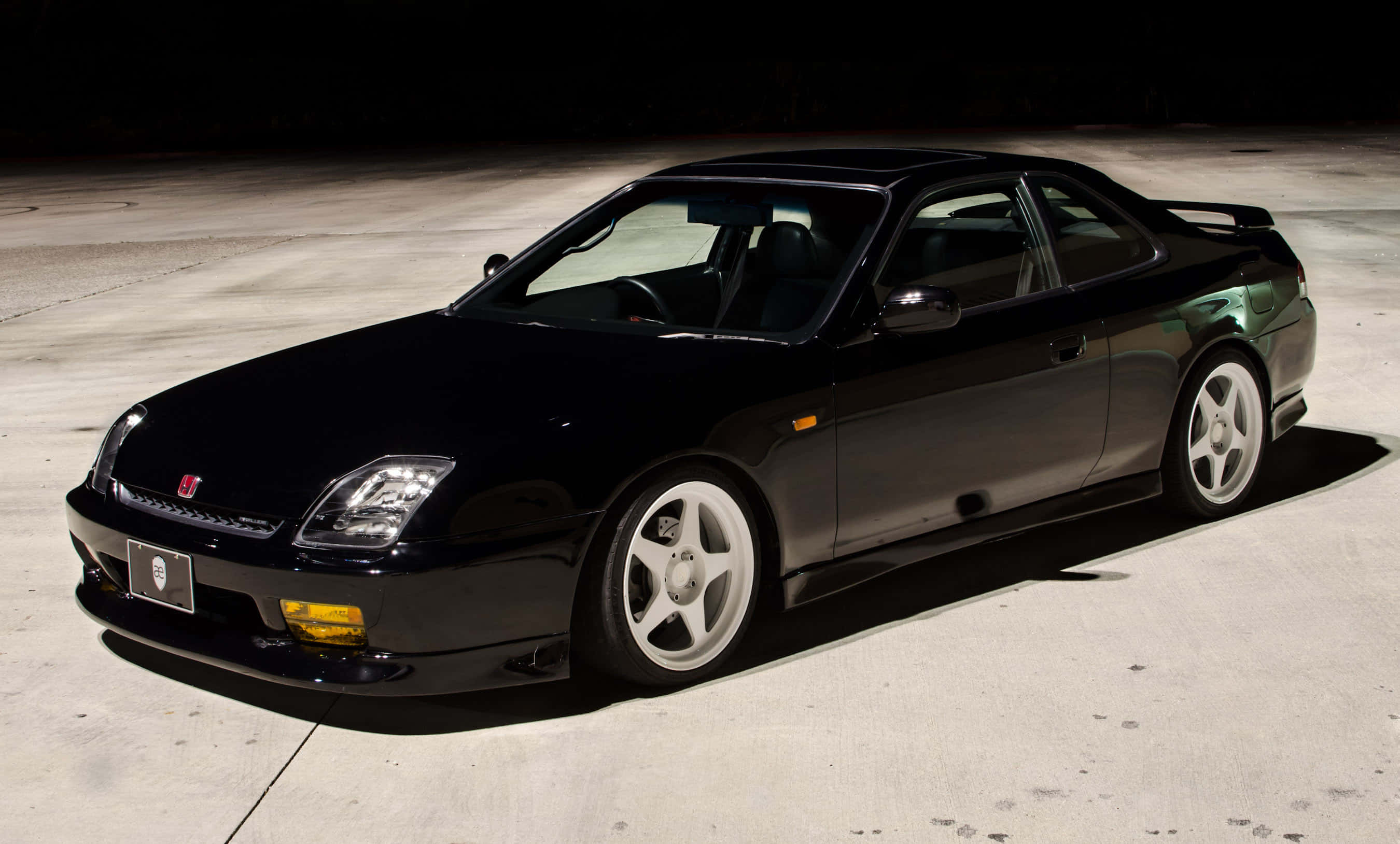 Honda Prelude 桌布 壁紙 — 一輛時尚的黑色運動轎跑車配白色輪圈，在工作室燈光下於混凝土地板上閃閃發光。
