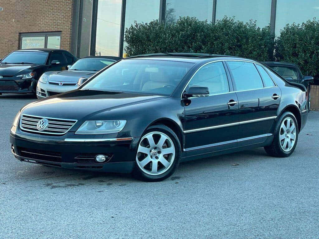  壁紙 — 一輛時尚的黑色福士Phaeton房車停在瀝青路上，背景有其他汽車和一棟磚砌建築。