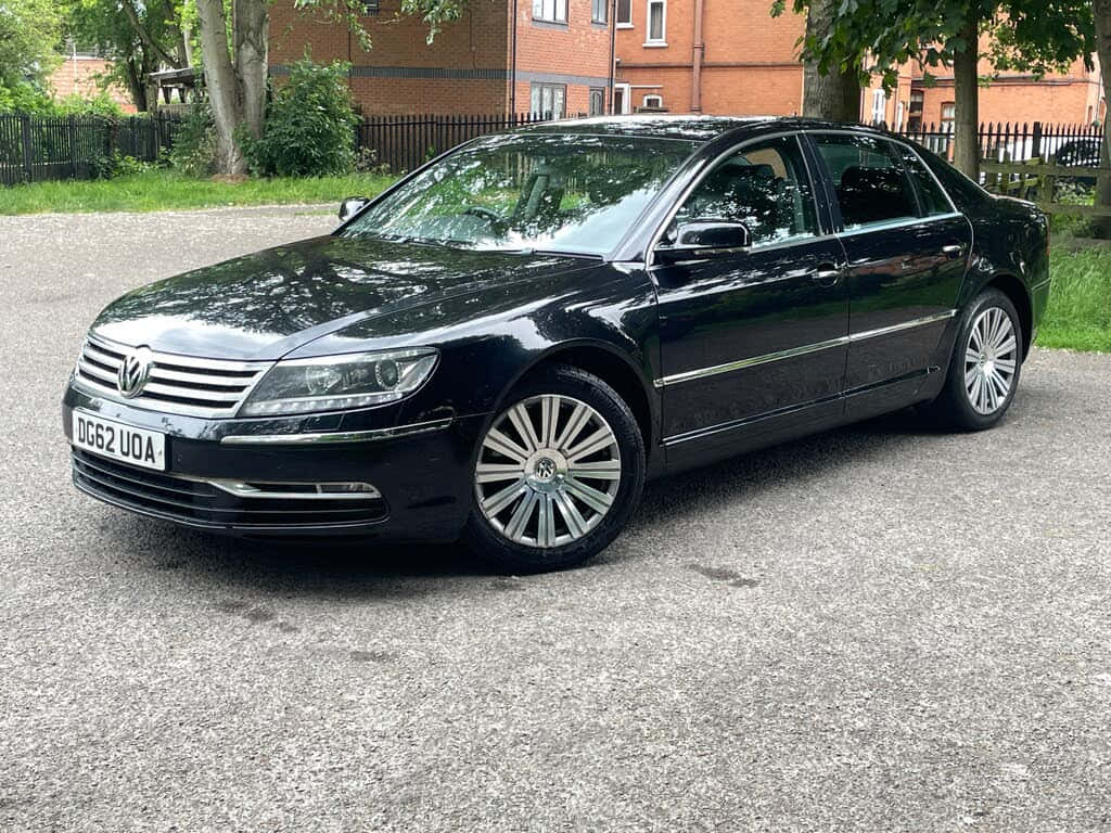  壁紙 — 一輛時尚的黑色福士偉根Phaeton房車停在碎石路上，背景有樹木和磚建築。