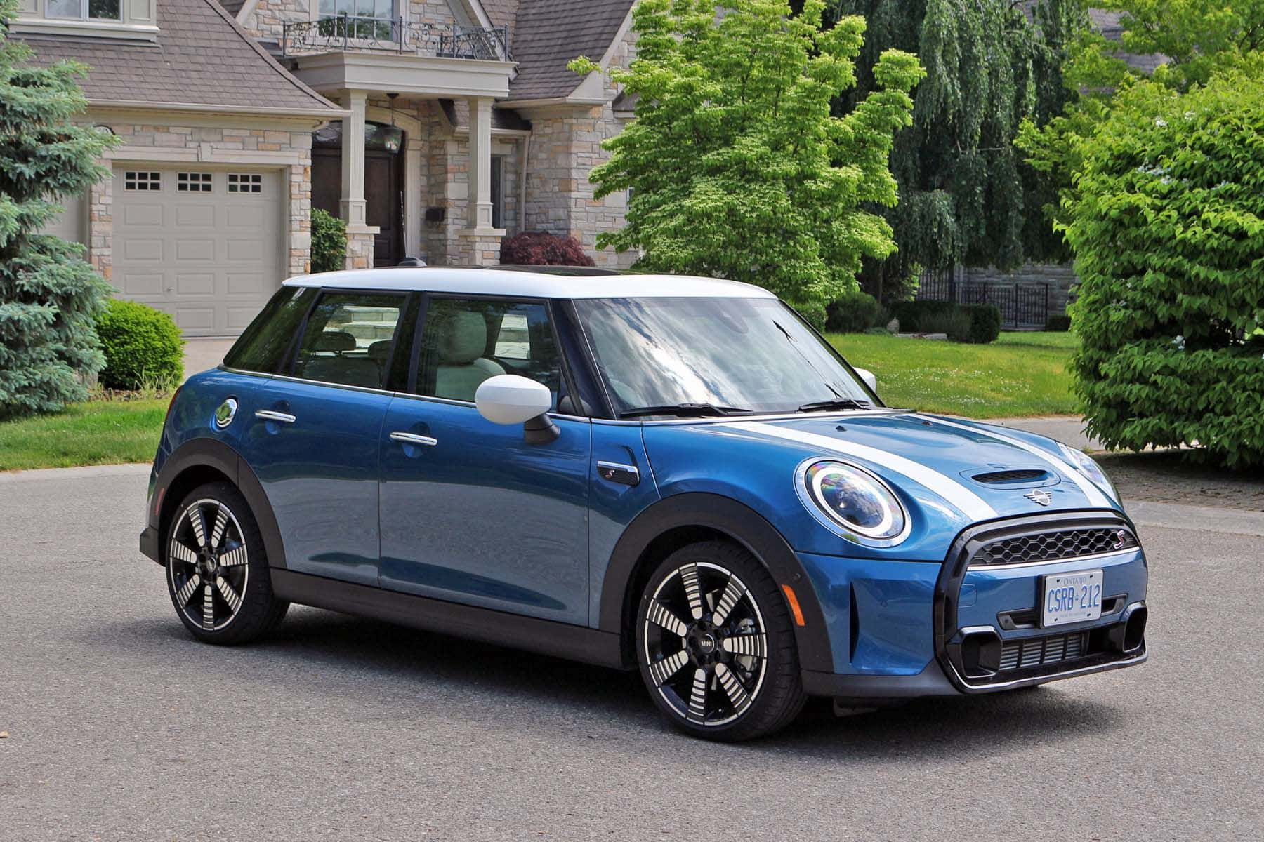 Mini Cooper S 桌布 壁紙 — 一架時尚的藍色電動MINI Cooper停泊在郊區車道上，旁邊是石屋和茂密的綠樹。