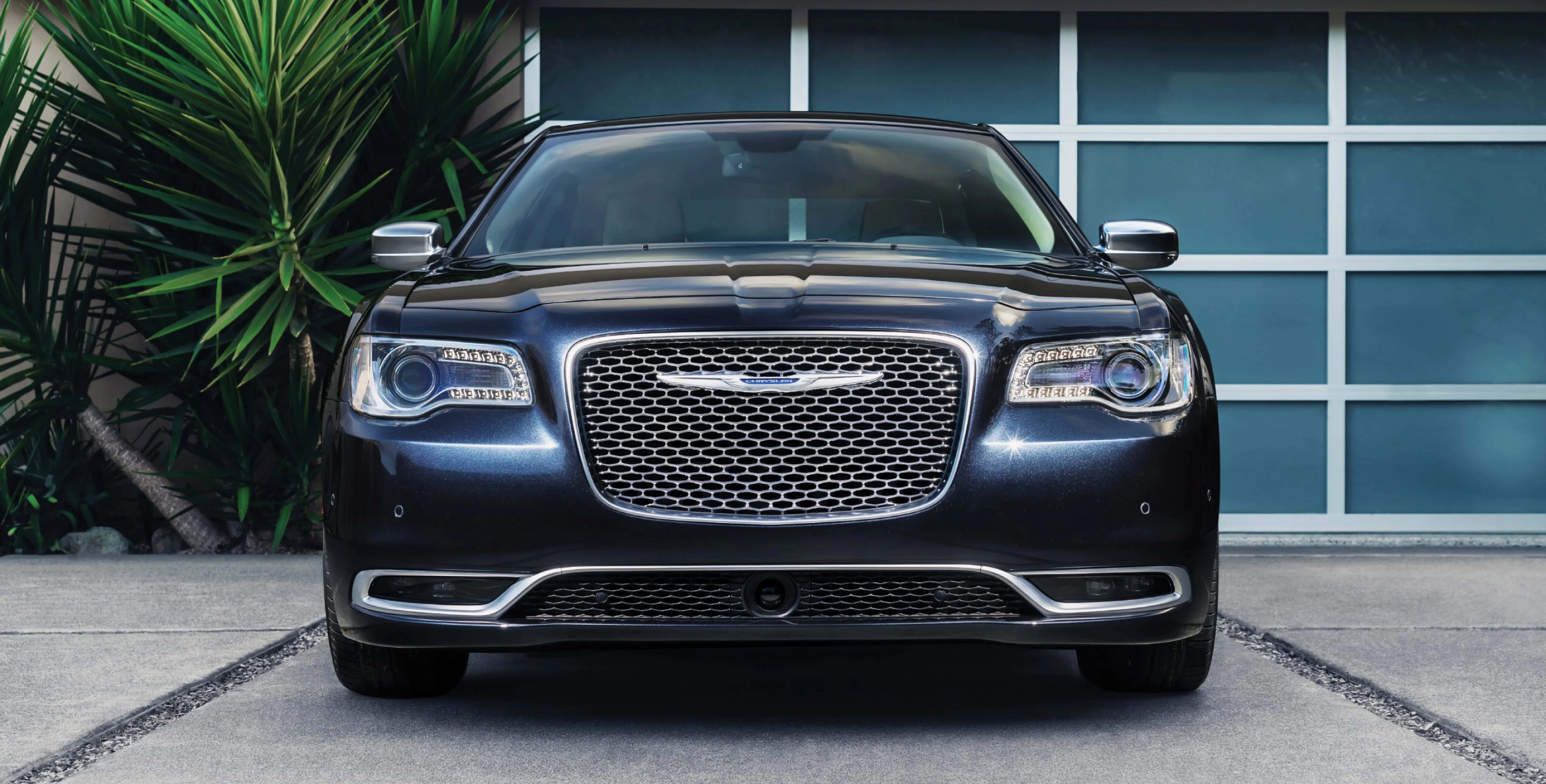 Chrysler 300 桌布 壁紙 — 一架時尚深藍色克萊斯勒300轎車面向現代藍色車庫門，旁邊有茂密的綠色棕櫚樹。