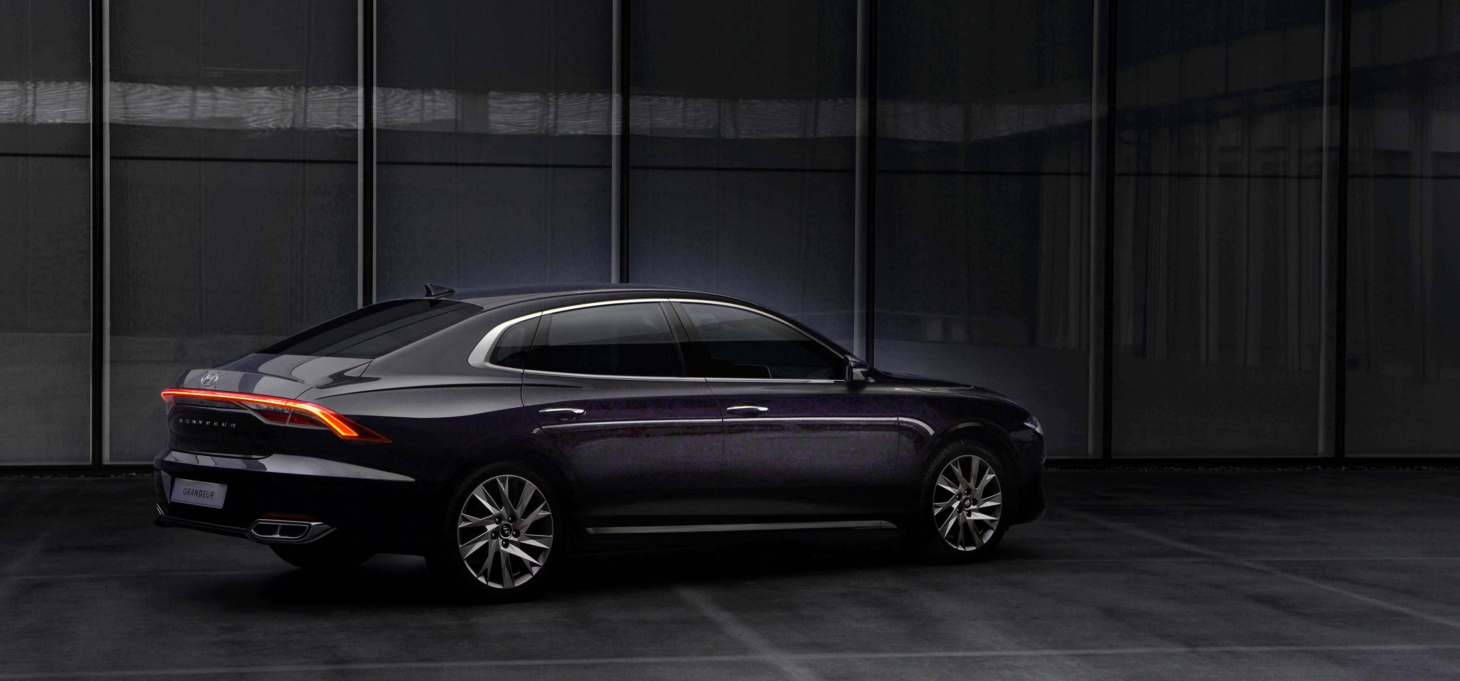 Hyundai Azera 桌布 壁紙 — 一架時尚深色轎車帶有發光尾燈，在簡約都市環境中停靠於現代玻璃牆前。
