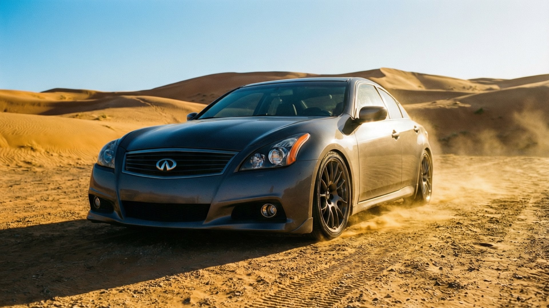 Infiniti G37 桌布 壁紙 — 一架時尚的灰色 Infiniti 房車在清澈藍天下，於金色沙漠沙丘上疾馳，揚起沙塵。