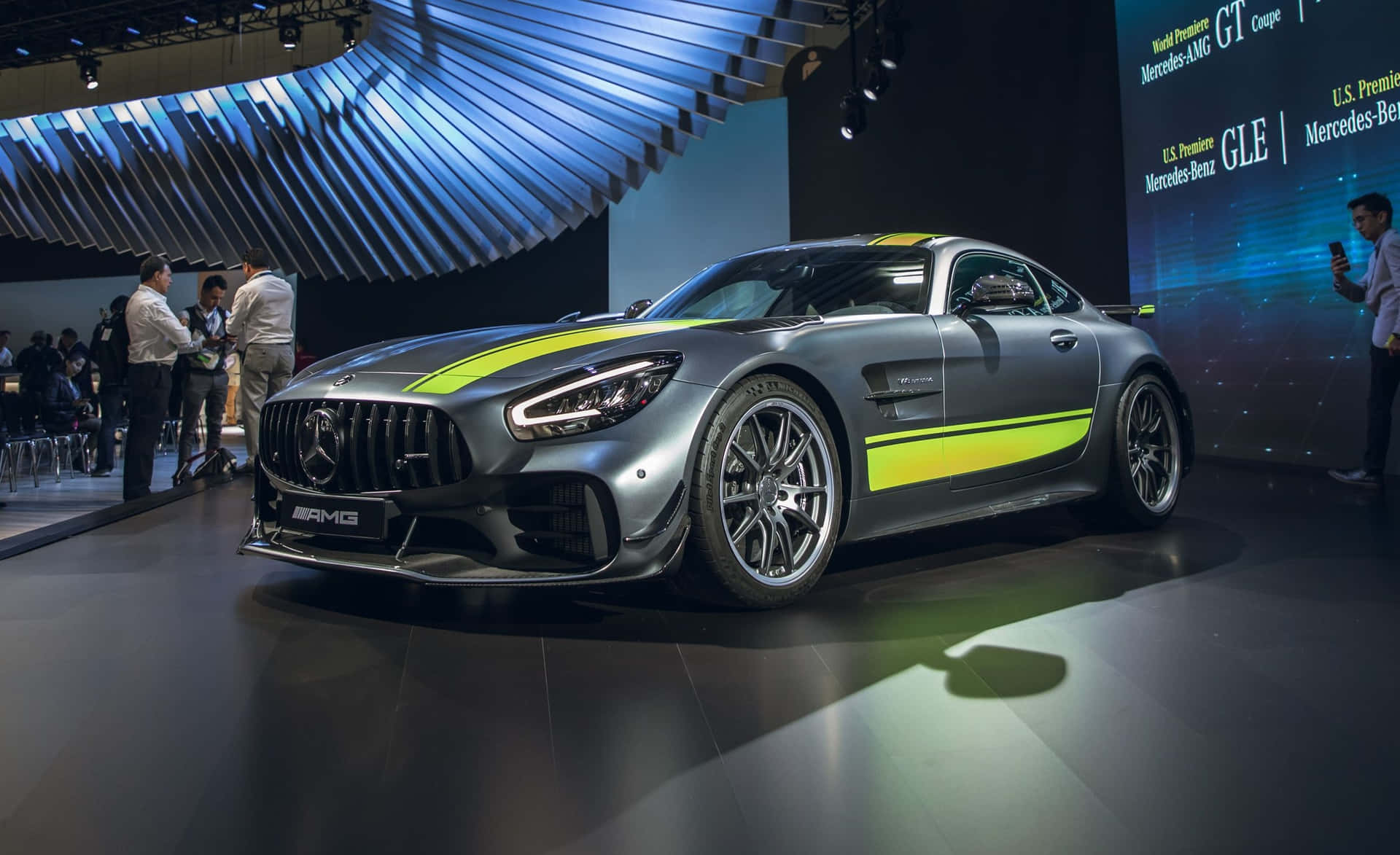  壁紙 — 一輛時尚的銀色 Mercedes-AMG GT Coupe 帶有螢光綠色條紋，在車展的聚光燈下閃閃發光。
