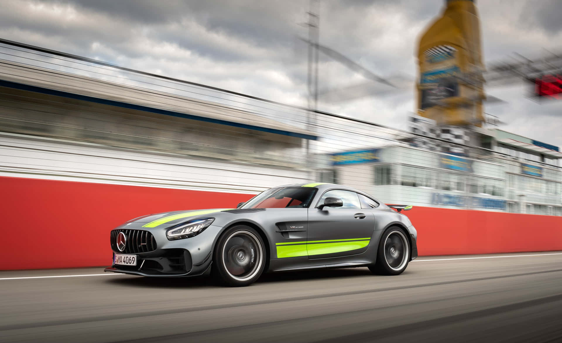  壁紙 — 一輛時尚的銀色Mercedes-AMG GT R，帶有螢光綠色點綴，在賽道上奔馳，呈現動態模糊效果和紅色護欄。