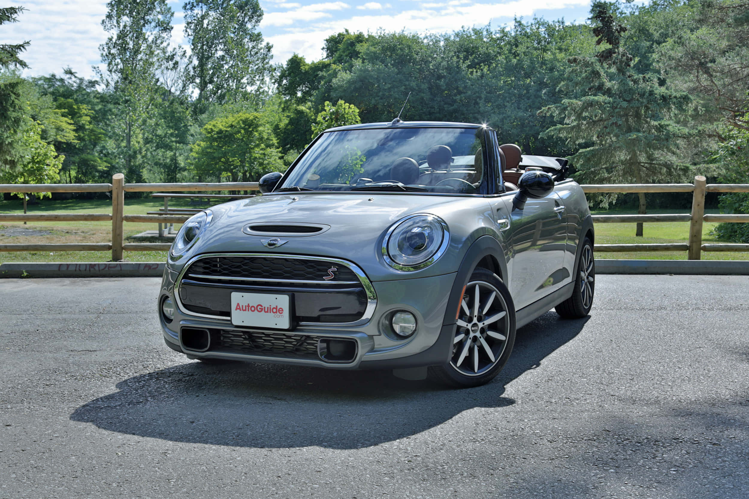 Mini Cooper S Convertible 桌布 壁紙 — 一輛時尚的銀色MINI Cooper開篷車停在瀝青路上，背景有茂密的綠樹和木柵欄，在明亮的日光下。