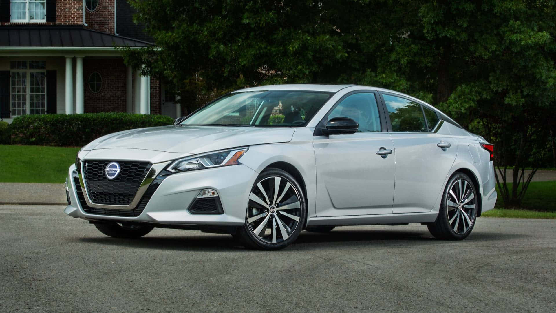 Nissan Altima 桌布 壁紙 — 一輛時尚的銀色日產Altima房車停在磚房前的車道上，周圍有茂密的綠樹。