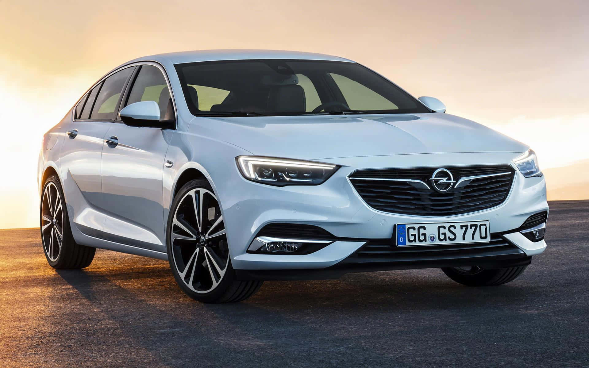 Opel Insignia 桌布 壁紙 — 一輛時尚的銀色歐寶轎車在平滑的瀝青路面上，於溫暖的黃金時段光線下閃閃發光。