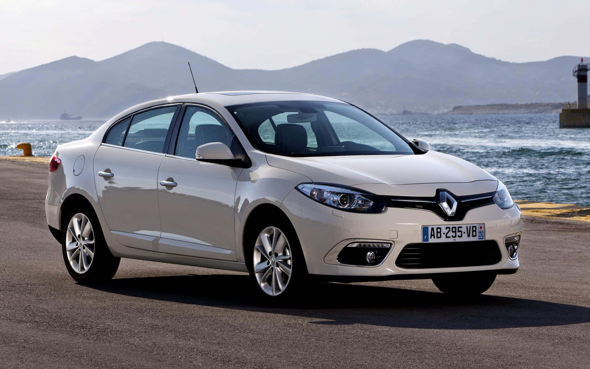 Renault Fluence 桌布 壁紙 — 一架時尚的銀色雷諾轎車停泊在沿海公路上，背景是山脈和海洋。