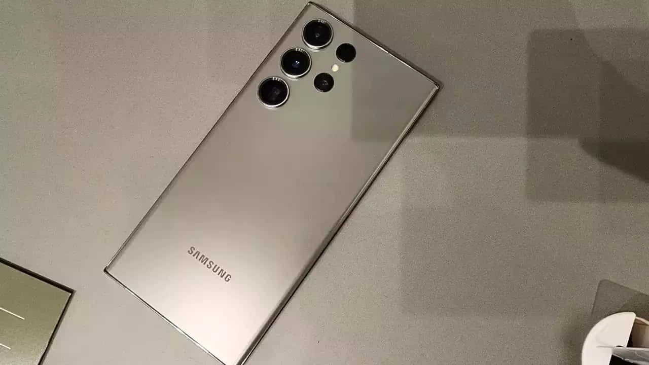 Samsung S23 Ultra 桌布 壁紙 — 一部時尚的銀色Samsung智能手機，配備四鏡頭陣列，對角放置在簡約的灰色表面上。