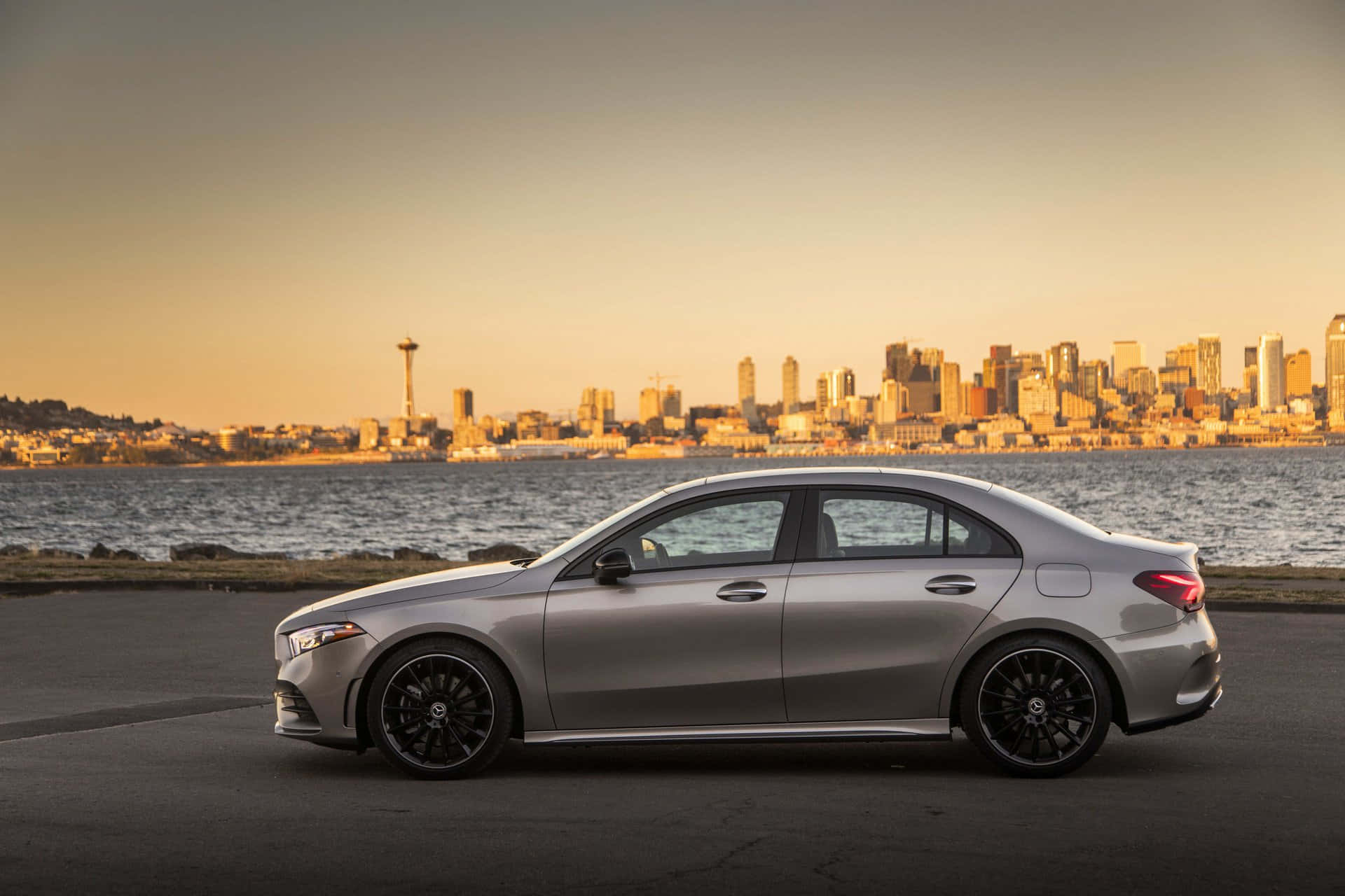 Mercedes Benz A-class 桌布 壁紙 — 一輛時尚的銀色轎車停在水邊，西雅圖天際線和太空針塔在金色日落光芒中閃耀。