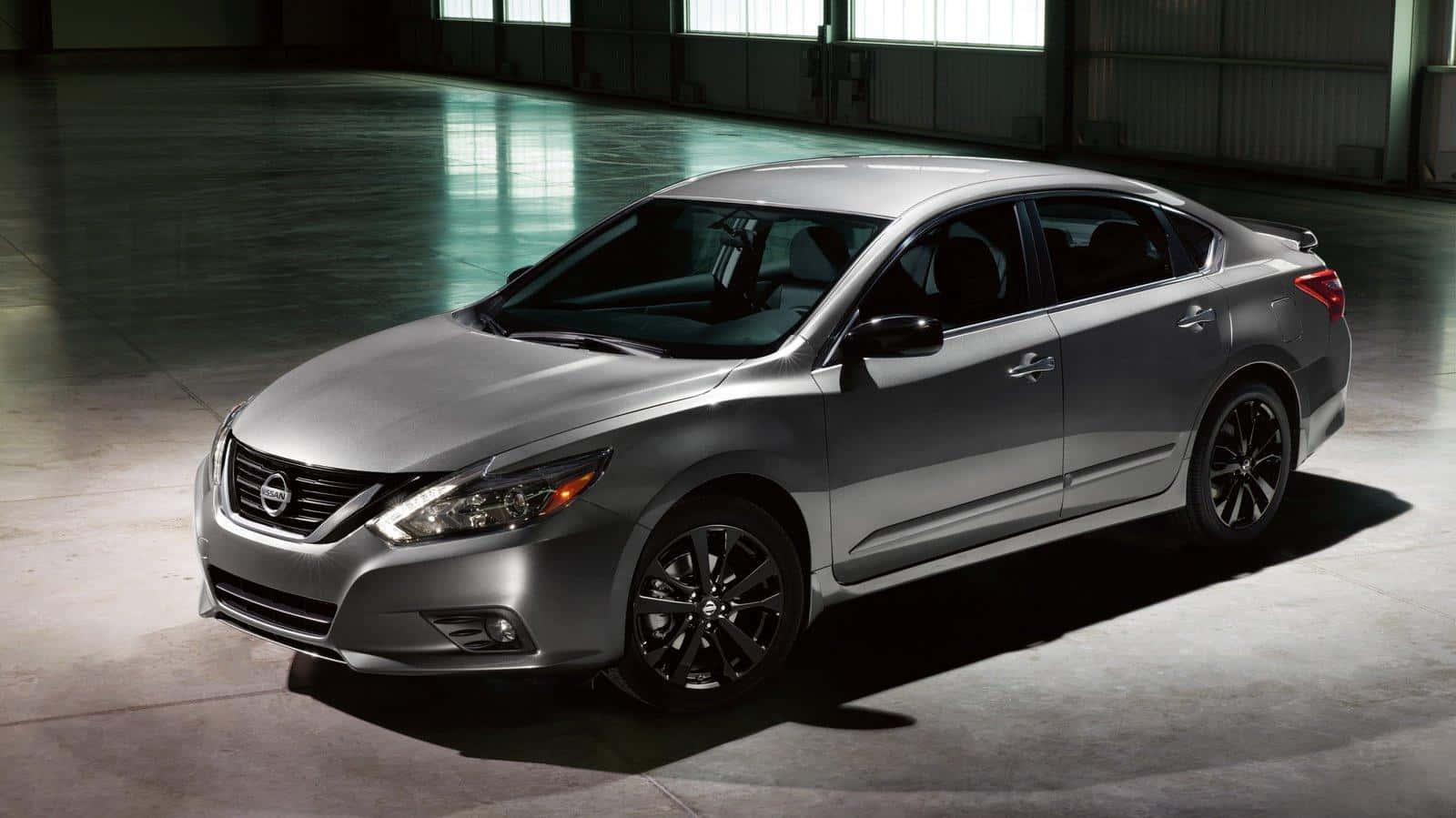 Nissan Altima 桌布 壁紙 — 一輛時尚的銀色轎車配黑色輪圈，在寬敞的工業倉庫中於戲劇性燈光下展示。