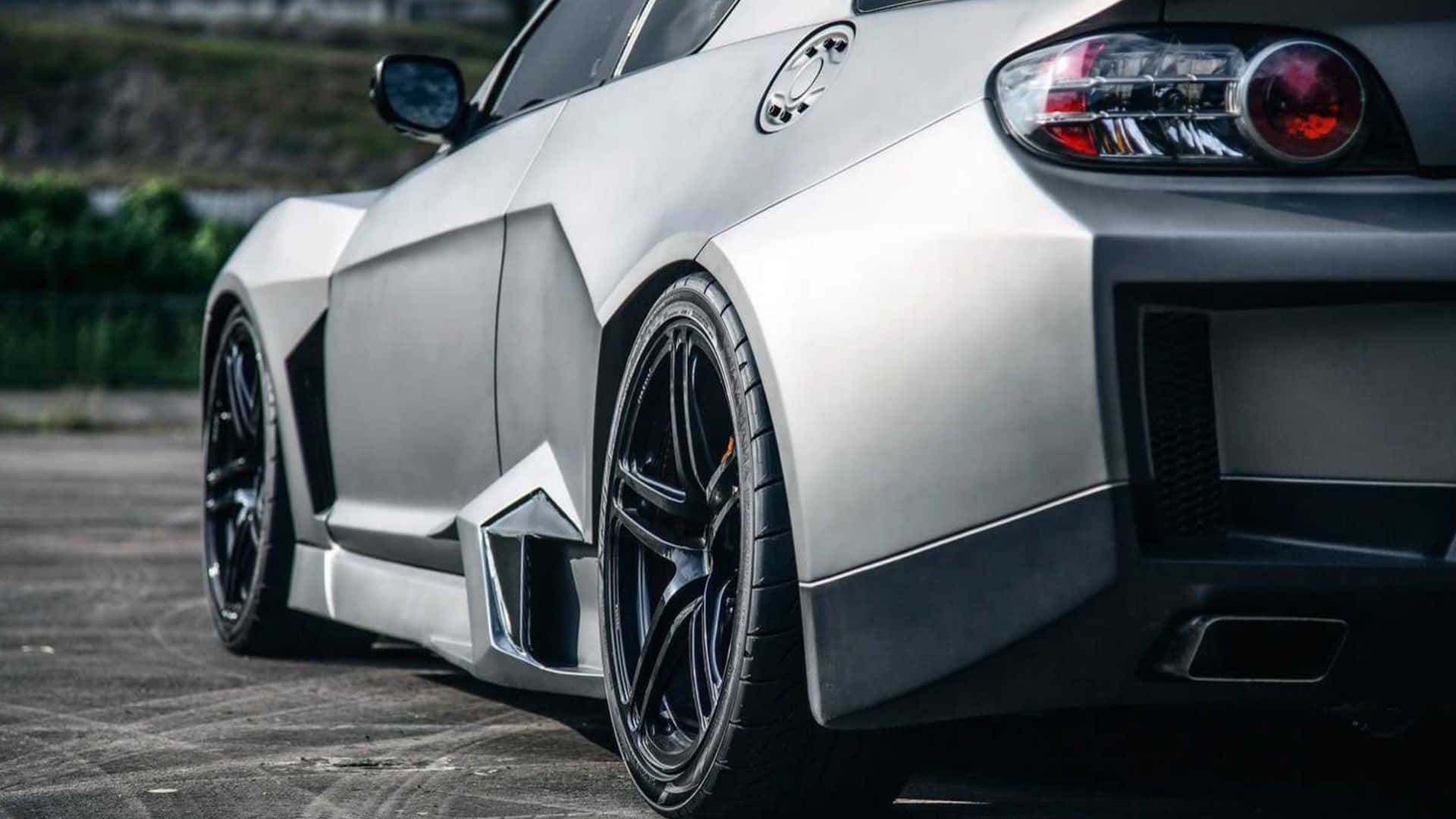 Mazda Rx-8 桌布 壁紙 — 一架時尚的銀色跑車，配備黑色輪圈和紅色尾燈，停泊在鋪砌路面上。