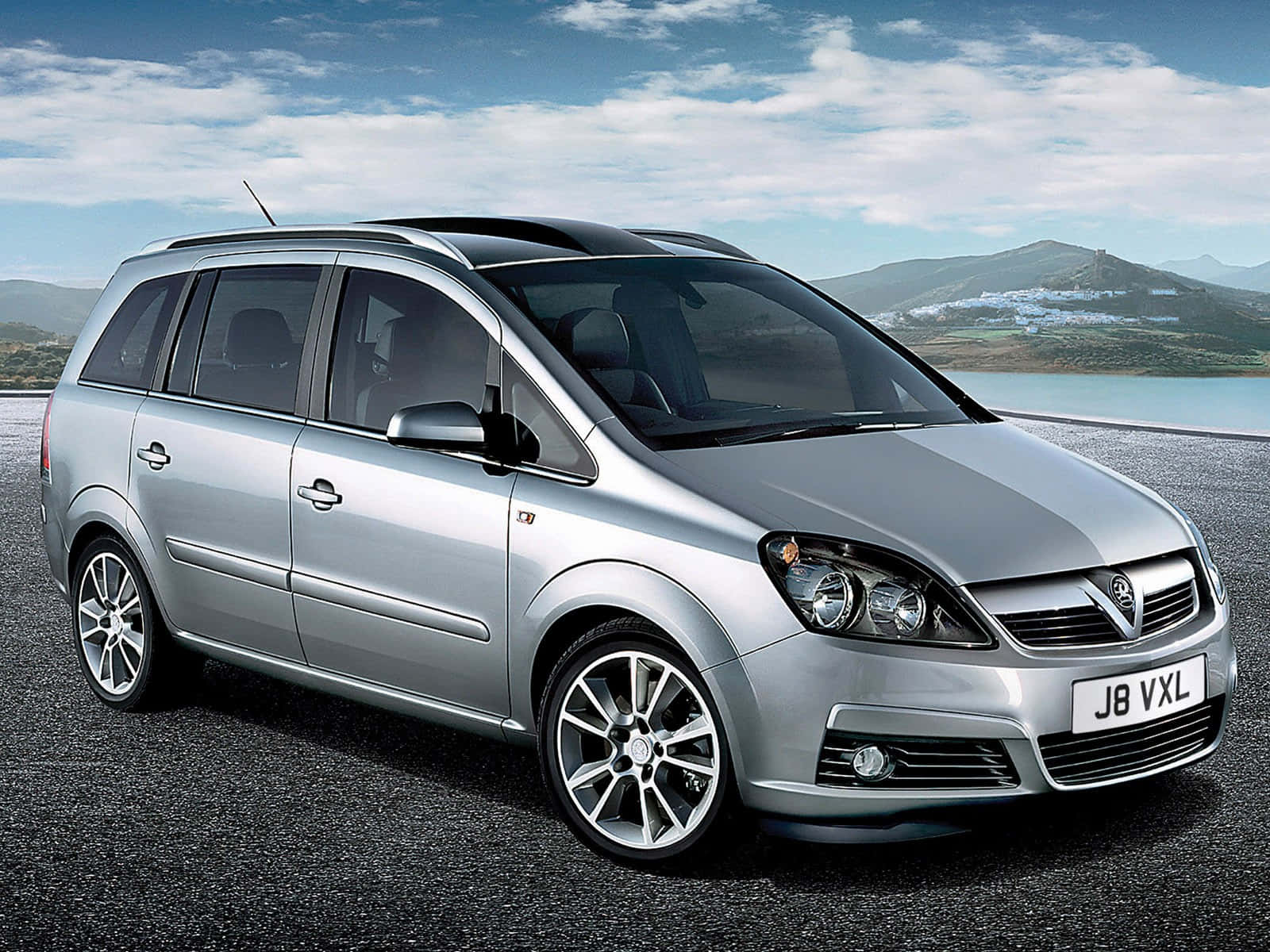 Opel Zafira 桌布 壁紙 — 一輛時尚的銀色Vauxhall Zafira停在瀝青路上，背景是山脈和湖泊，天空部分多雲。