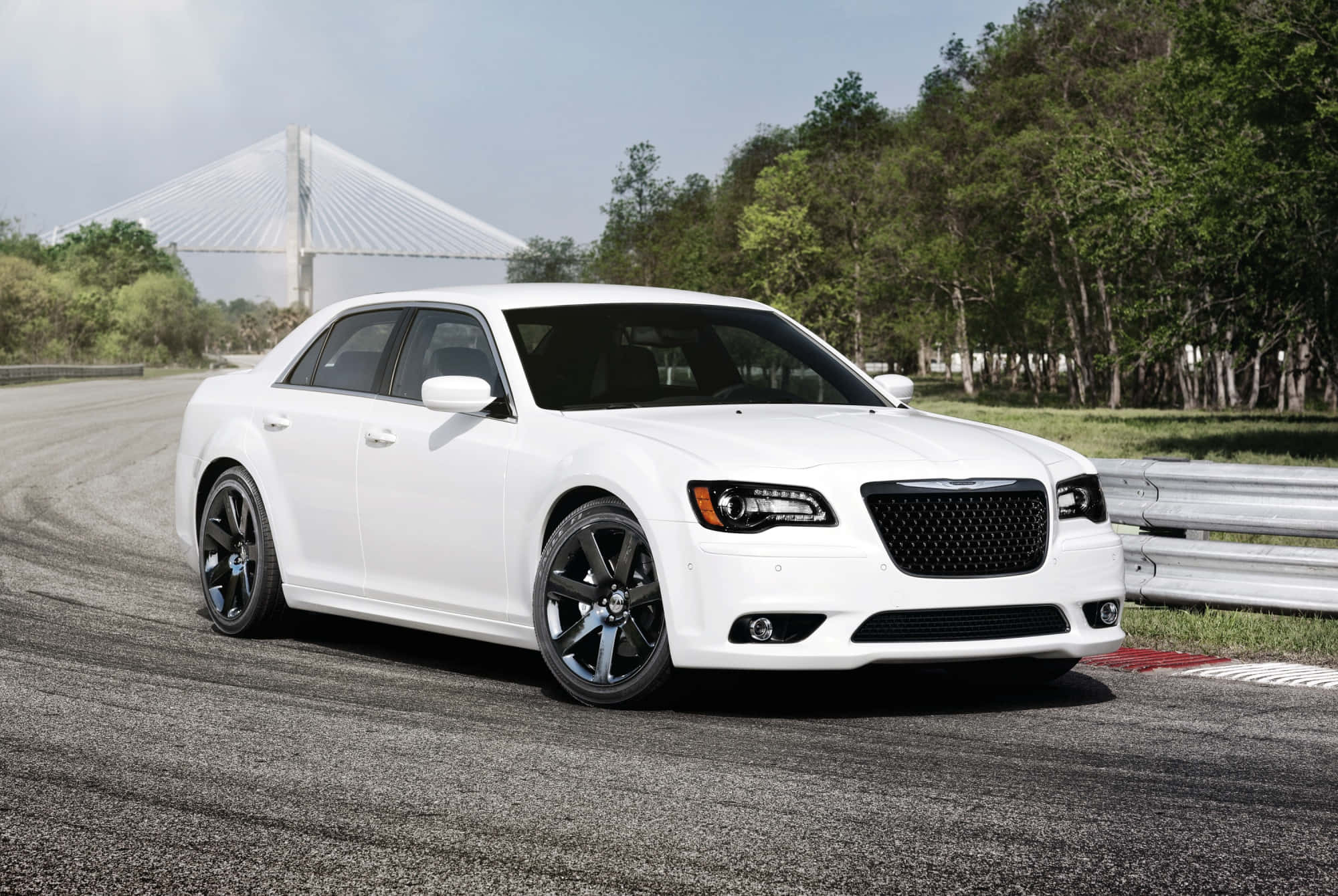 Chrysler 300 桌布 壁紙 — 一輛時尚的白色轎車配黑色輪圈，停在賽道上，旁邊是森林區域和一座現代橋樑，天空明亮。