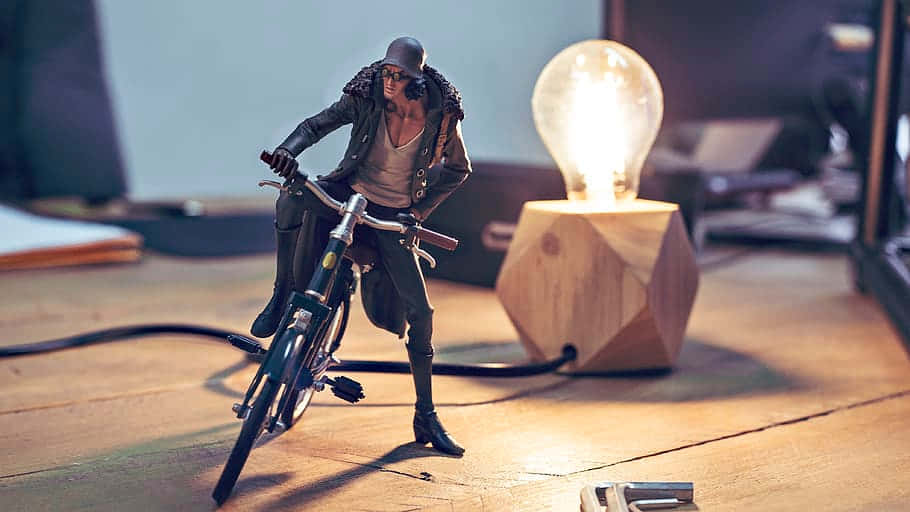 Aokiji 桌布 壁紙 — 一個風格化的動作人偶騎著單車，坐在木地板上一個發光的燈泡燈旁邊。