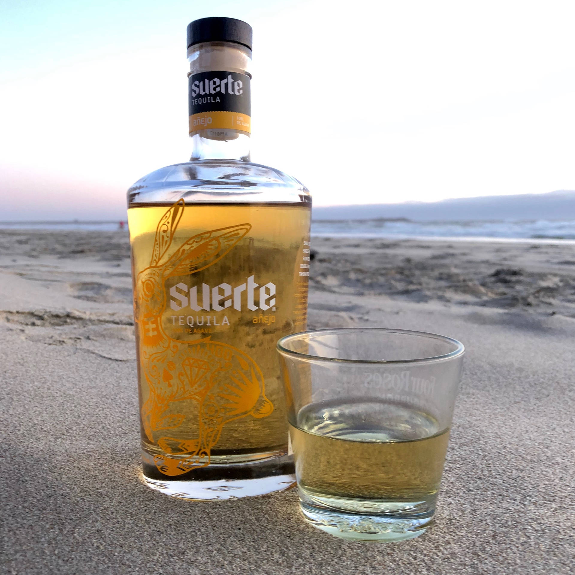 Suerte龍舌蘭酒瓶和玻璃杯在沙灘日落