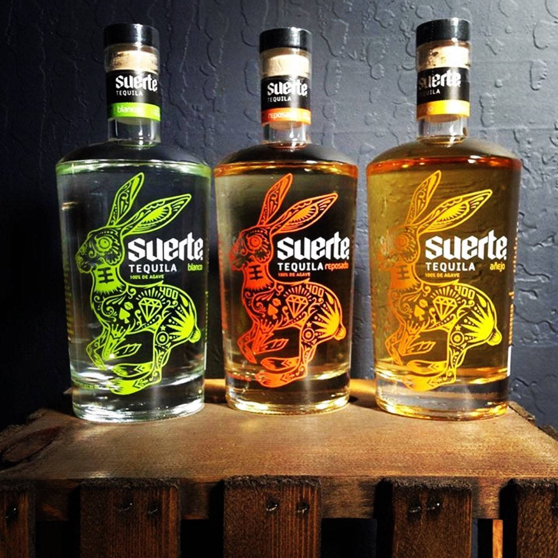 三瓶帶有兔子藝術的Suerte龍舌蘭酒瓶放在木質表面上。