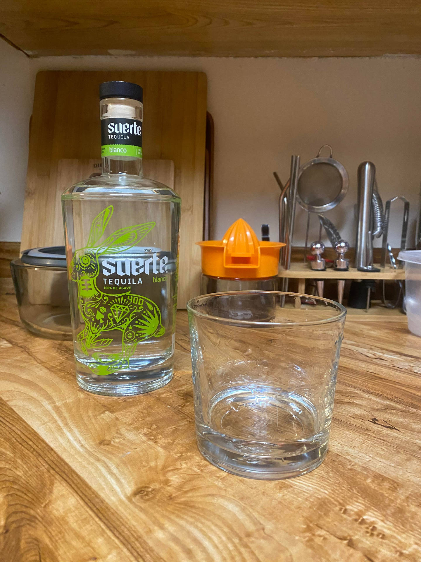 Suerte龍舌蘭酒瓶和玻璃杯在木製廚房檯面上，工具在後面。