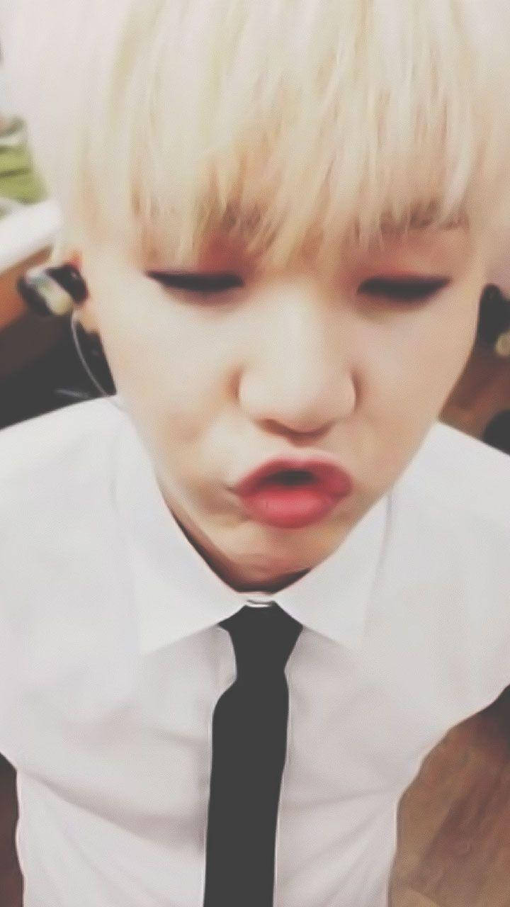 嘟嘴 Suga BTS 壁紙 — 一個擁有鉑金色頭髮和紅唇的人，穿著白襯衫和黑色領帶，做出俏皮的嘟嘴表情的特寫。