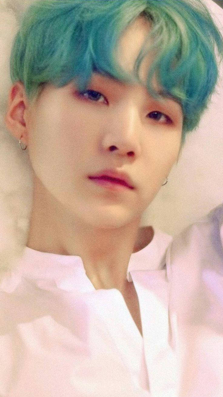 Suga BTS《Love Yourself: Her》概念照 壁紙 — 一位年輕男子的特寫肖像，擁有鮮豔的藍綠色頭髮和柔和粉紅燈光，身穿白色襯衫和小圈耳環。