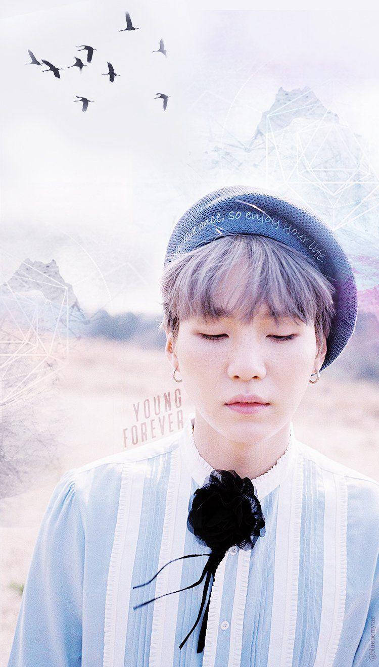 Suga BTS 紫色漸層髮型 壁紙 — 一個閉上眼睛的年輕人戴著藍色帽子和條紋襯衫，上面有黑色花朵，背景是夢幻的天空，有飛鳥和幾何山脈。