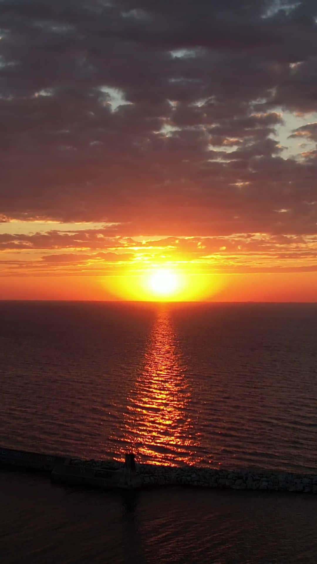 夕陽映照海洋，鮮豔的橙色和金色在平靜的水面上反射