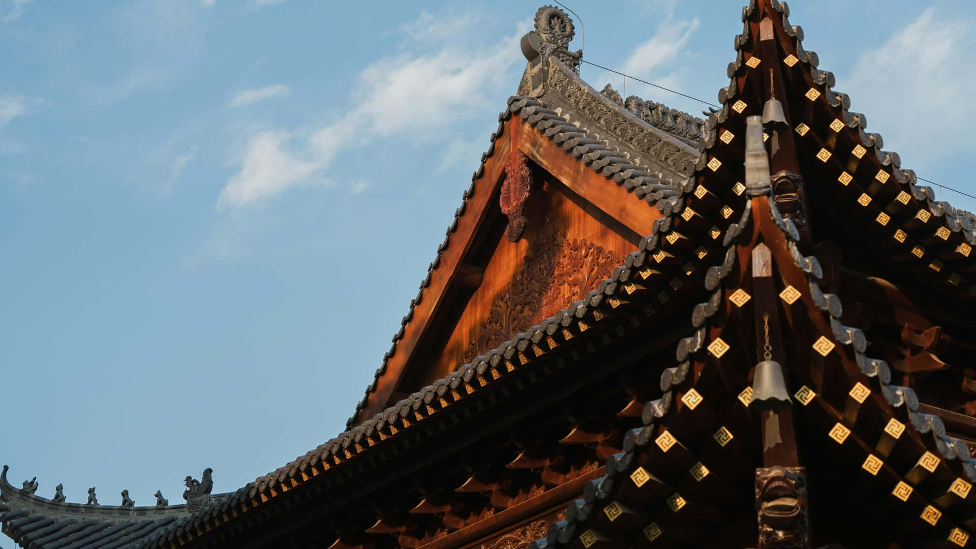  壁紙 — 陽光照射下的傳統中式寺廟屋頂，飾有華麗的木樑和金色點綴，襯托著清澈的藍天。