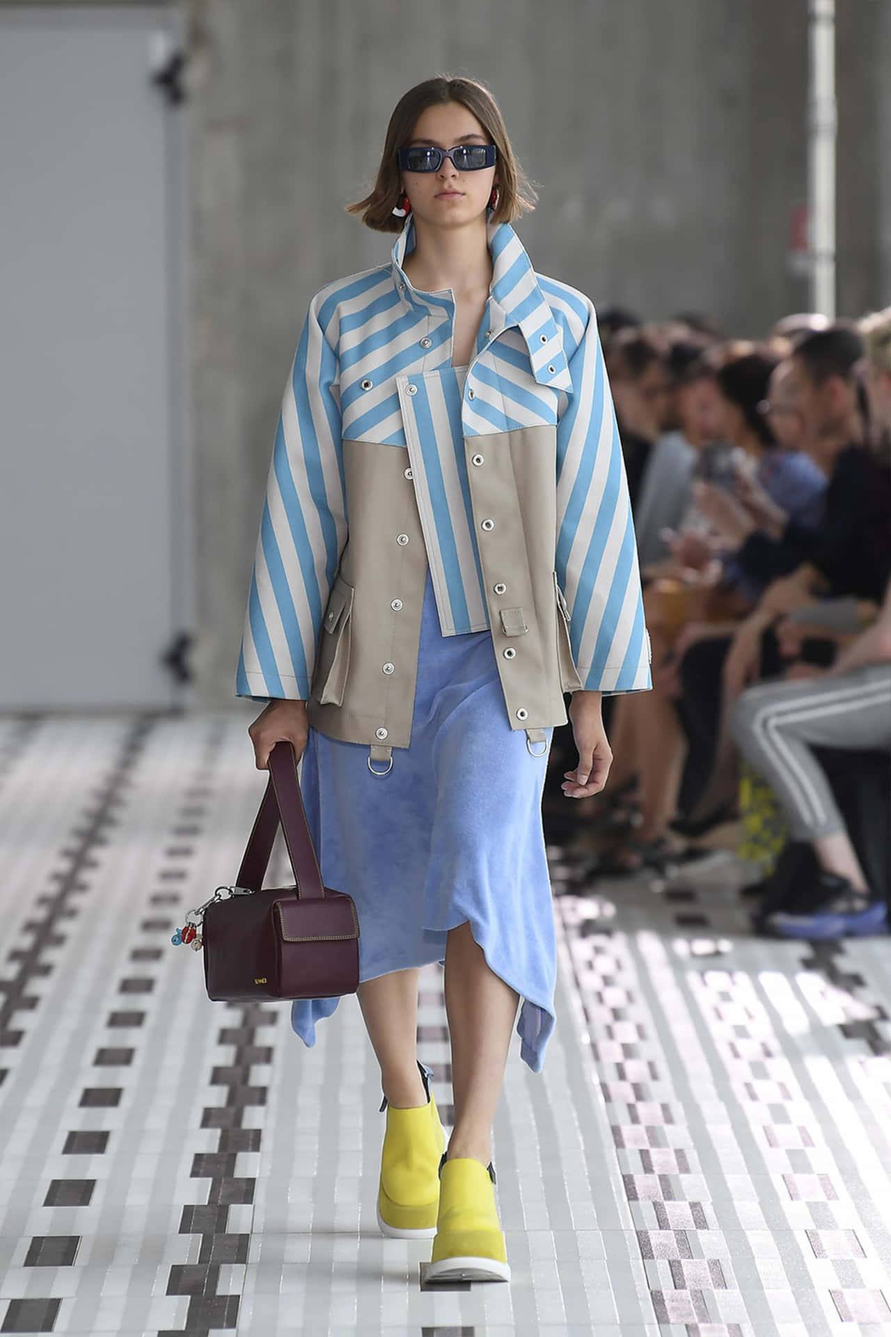模特兒身穿條紋外套、藍色裙子和黃色靴子走 runway。