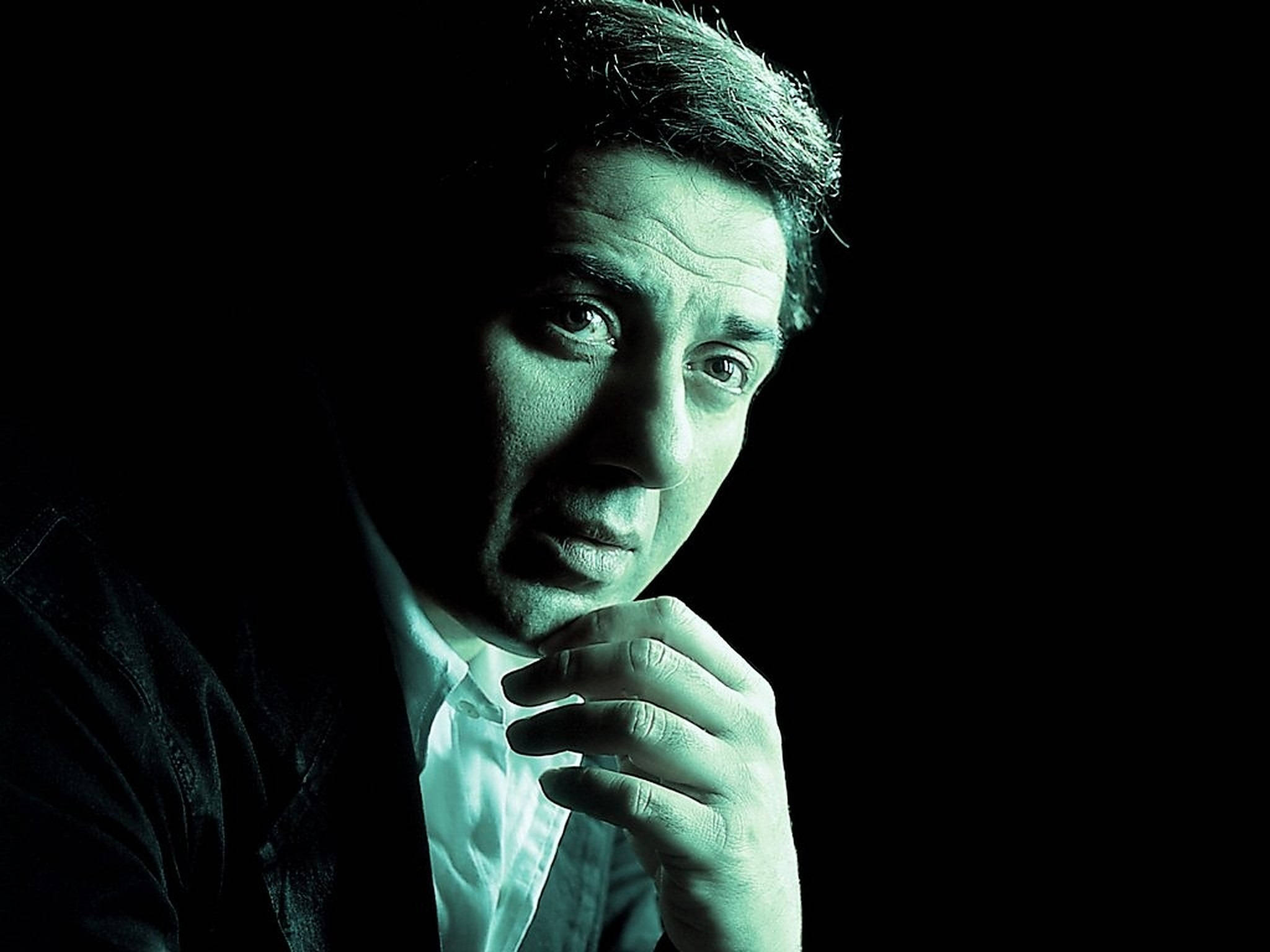 Sunny Deol 綠色濾鏡照 壁紙 — 一個穿著白色襯衫和深色外套的男人在戲劇性的綠色燈光下，對著黑色背景沉思地凝視。