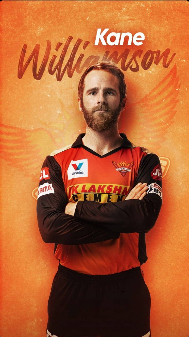 板球運動員 Kane Williamson 身穿球隊球衣，在橙色背景上雙臂交叉。