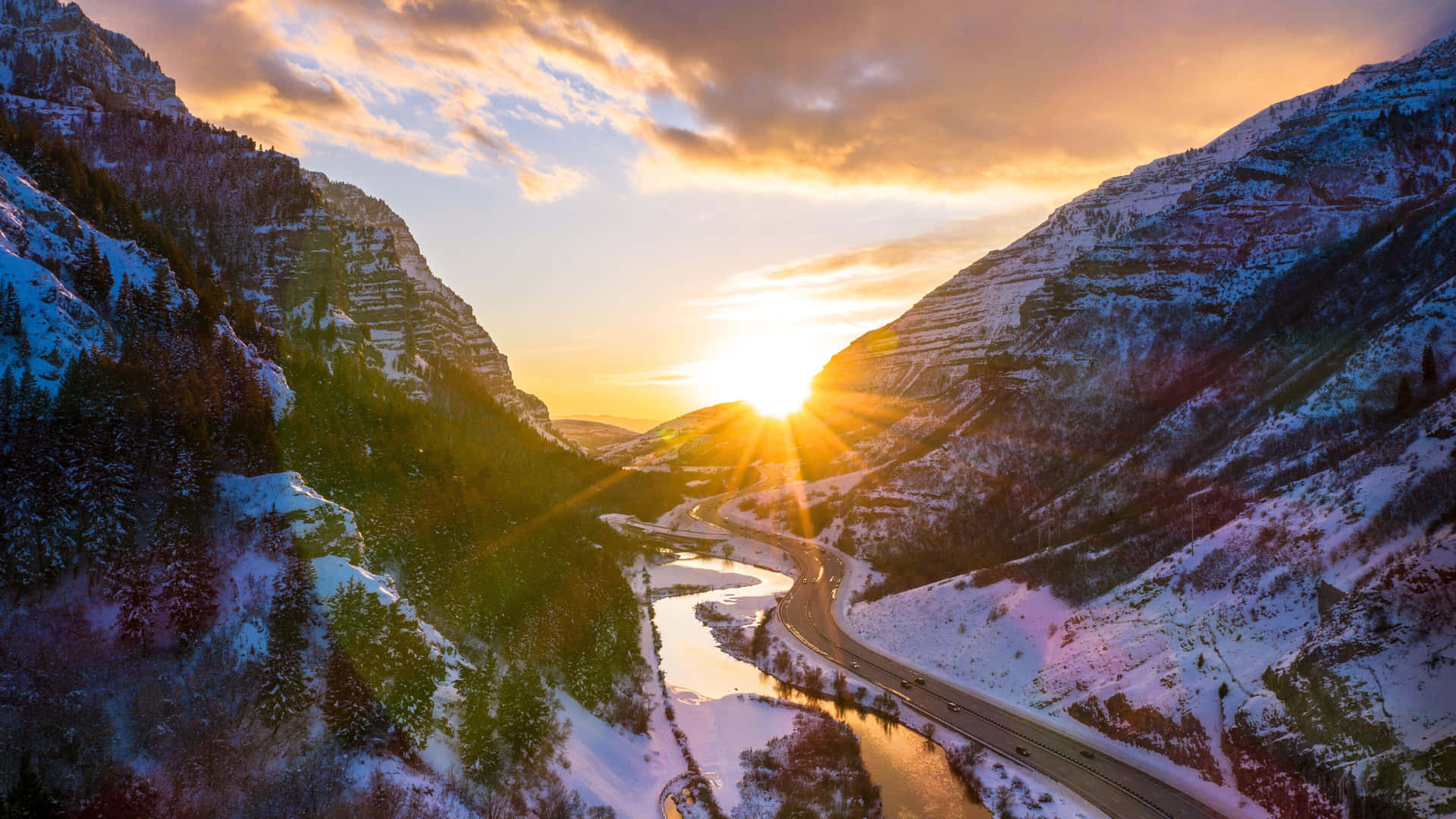  壁紙 — 夕陽穿過積雪的山峰閃耀，蜿蜒的道路和河流劃過下方的山谷。