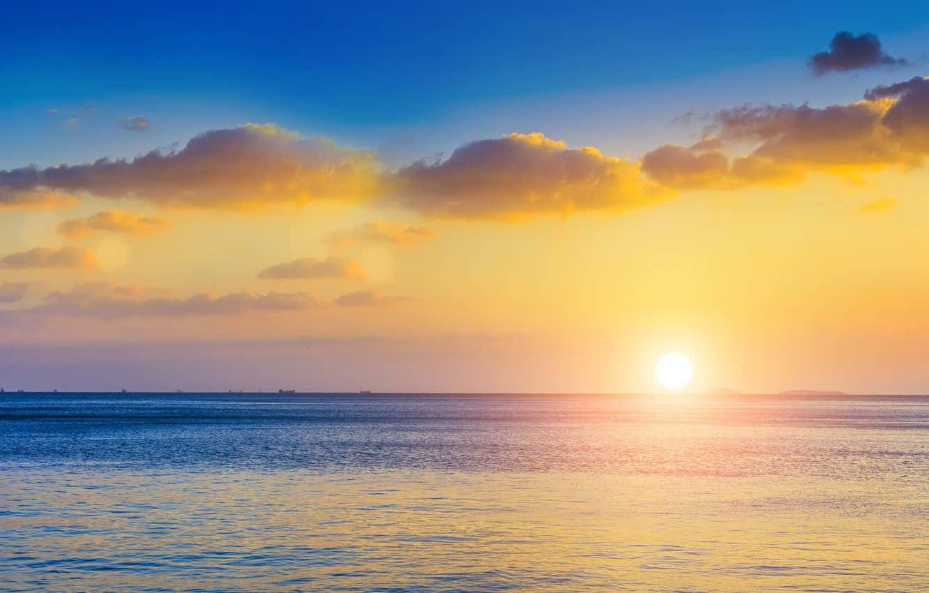 Sunset Hues 桌布 壁紙 — 平靜海洋上的日落，金色雲彩倒映在漣漪水面上，深藍天空下。