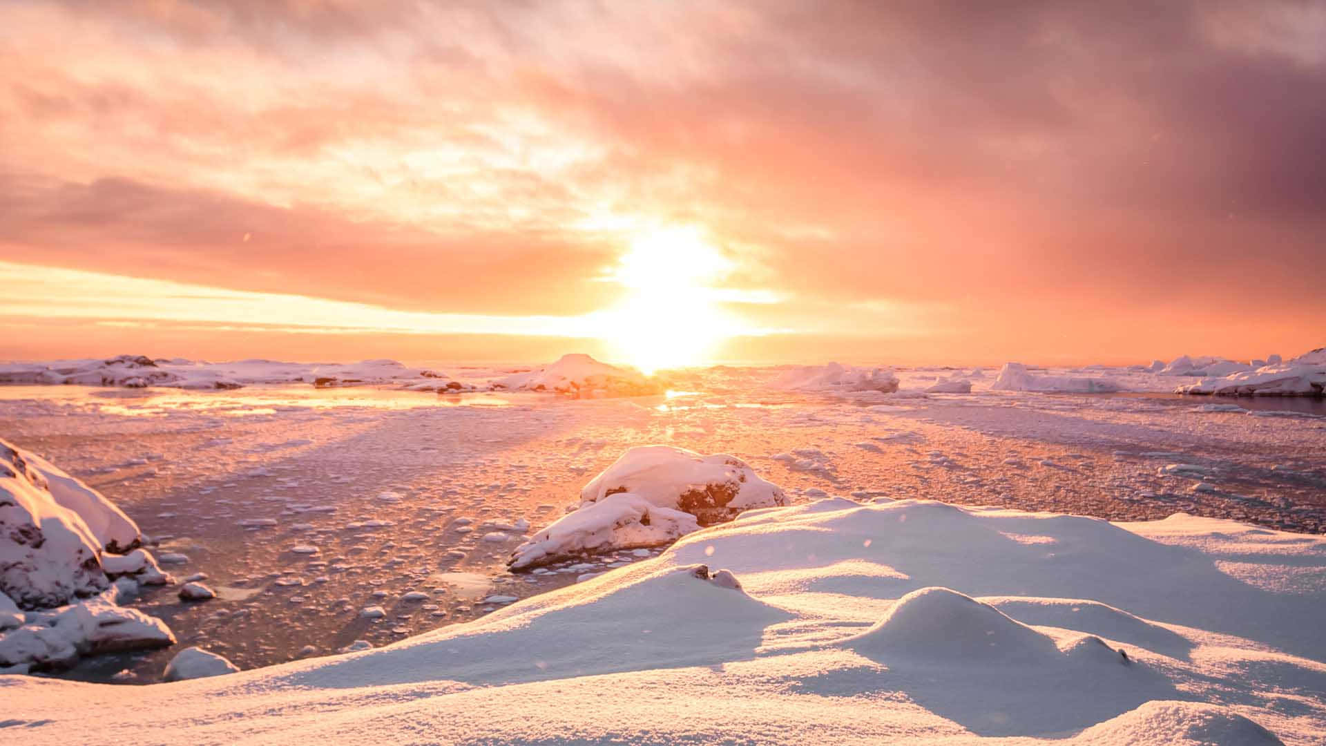 冰凍的北極海岸線沐浴在溫暖的夕陽光中，有積雪的岩石和浮冰。