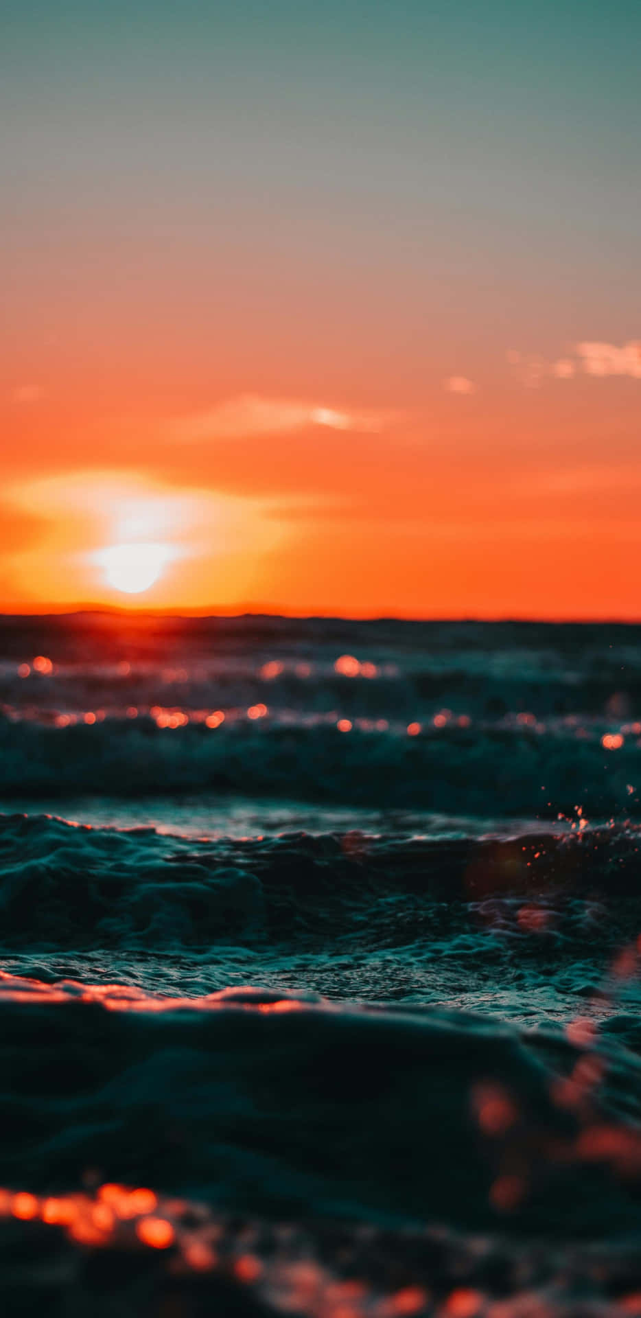  壁紙 — 夕陽將海洋染成火熱的橙色和藍綠色，海浪拍打時閃爍著粼粼波光。