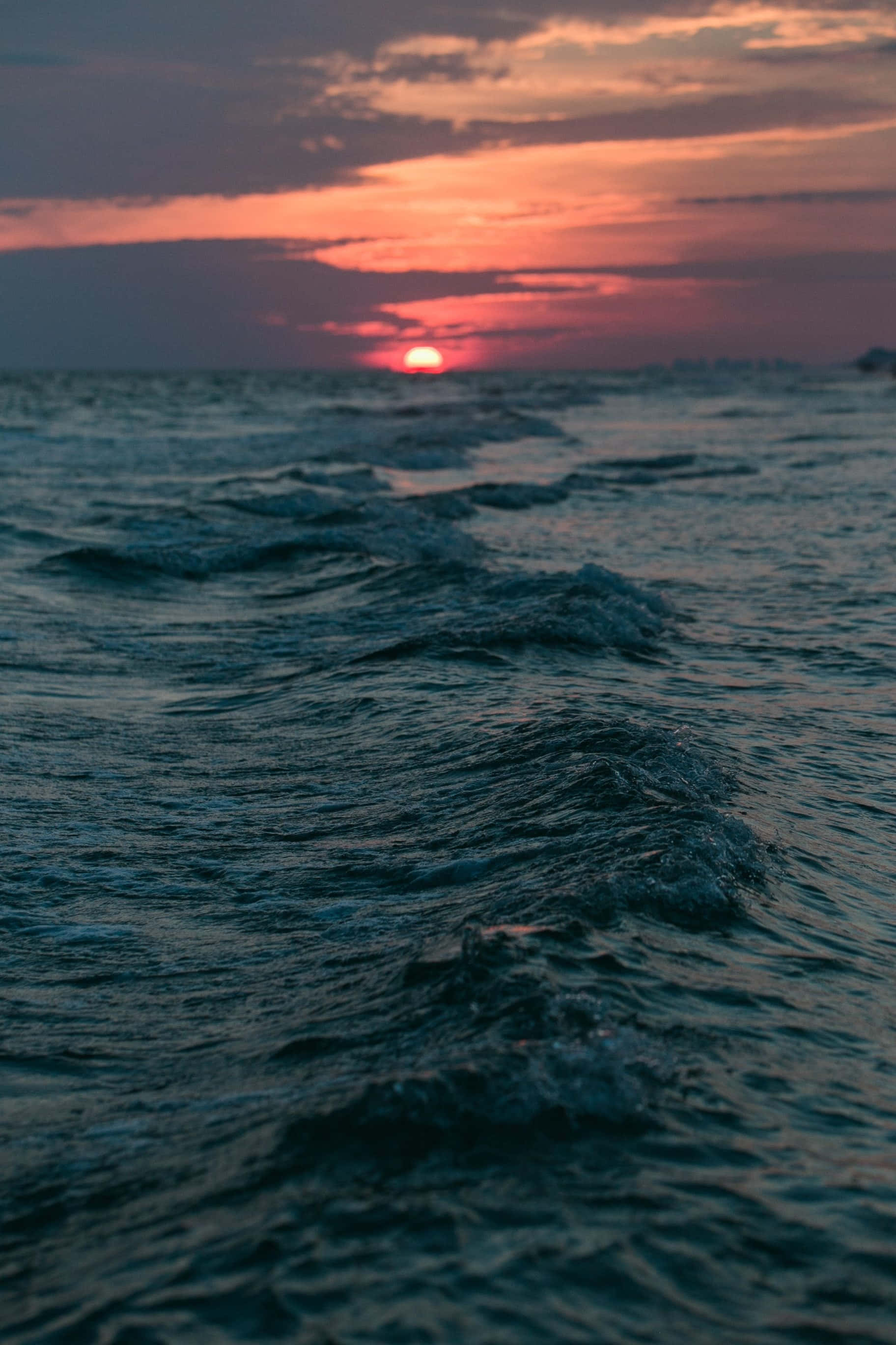 Sunset Ocean 桌布 壁紙 — 夕陽將天空染成火熱的橙色和粉紅色，波浪在海面上蕩漾。