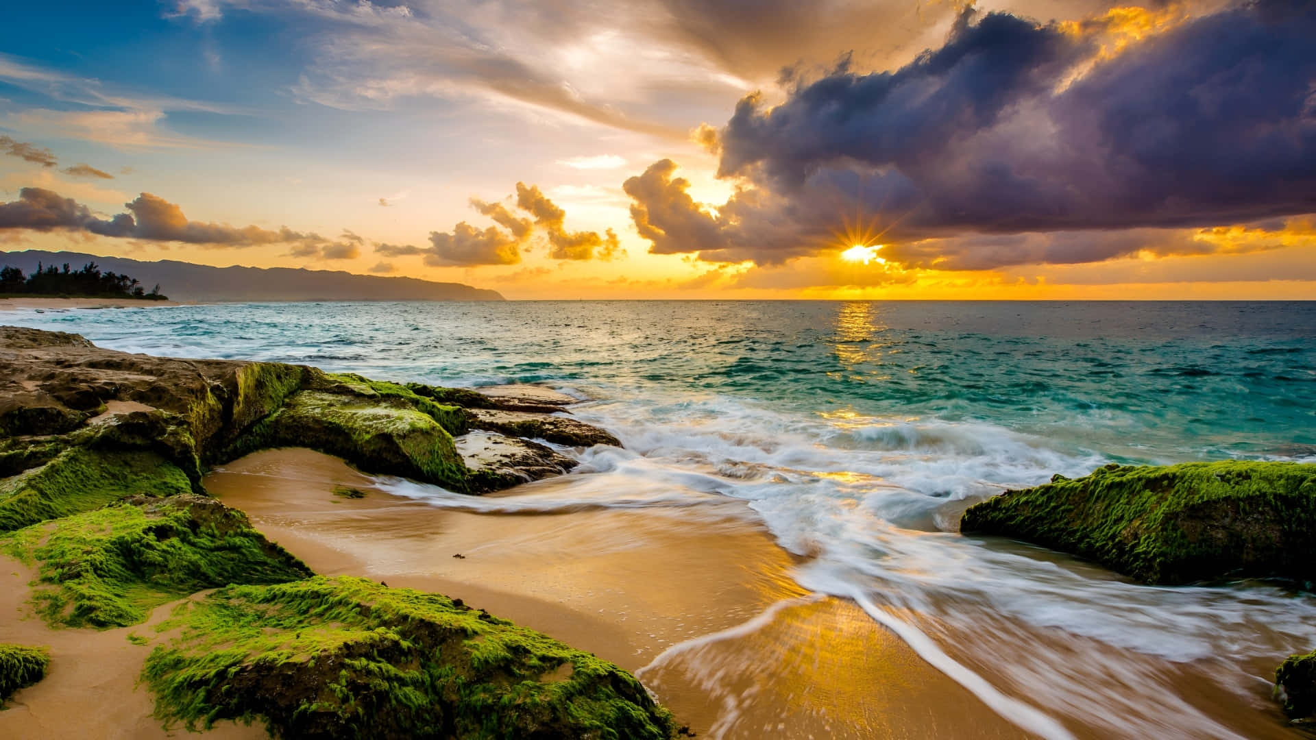  壁紙 — 夕陽將天空染成火熱的橙色和紫色，海浪拍打著熱帶海灘上長滿苔蘚的岩石。