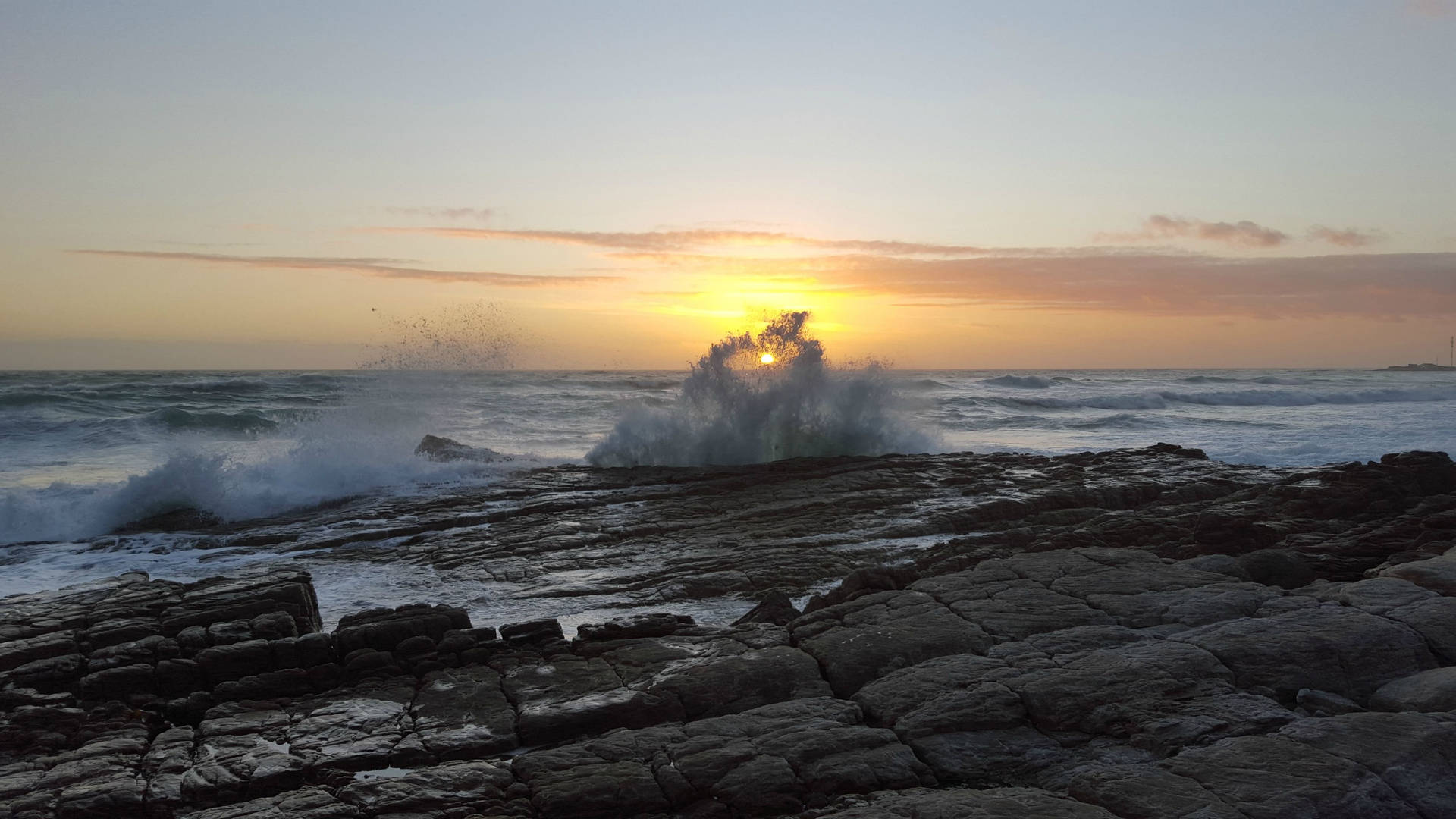 夕陽映照海洋，海浪拍打岩石海岸。