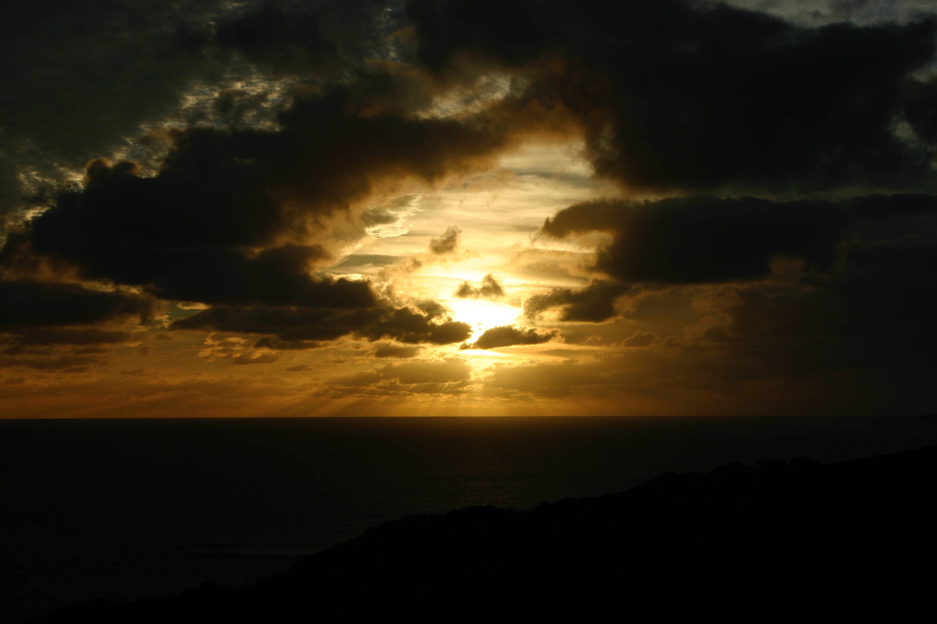 夕陽的金色光芒穿透海洋和山丘上方的暗雲。