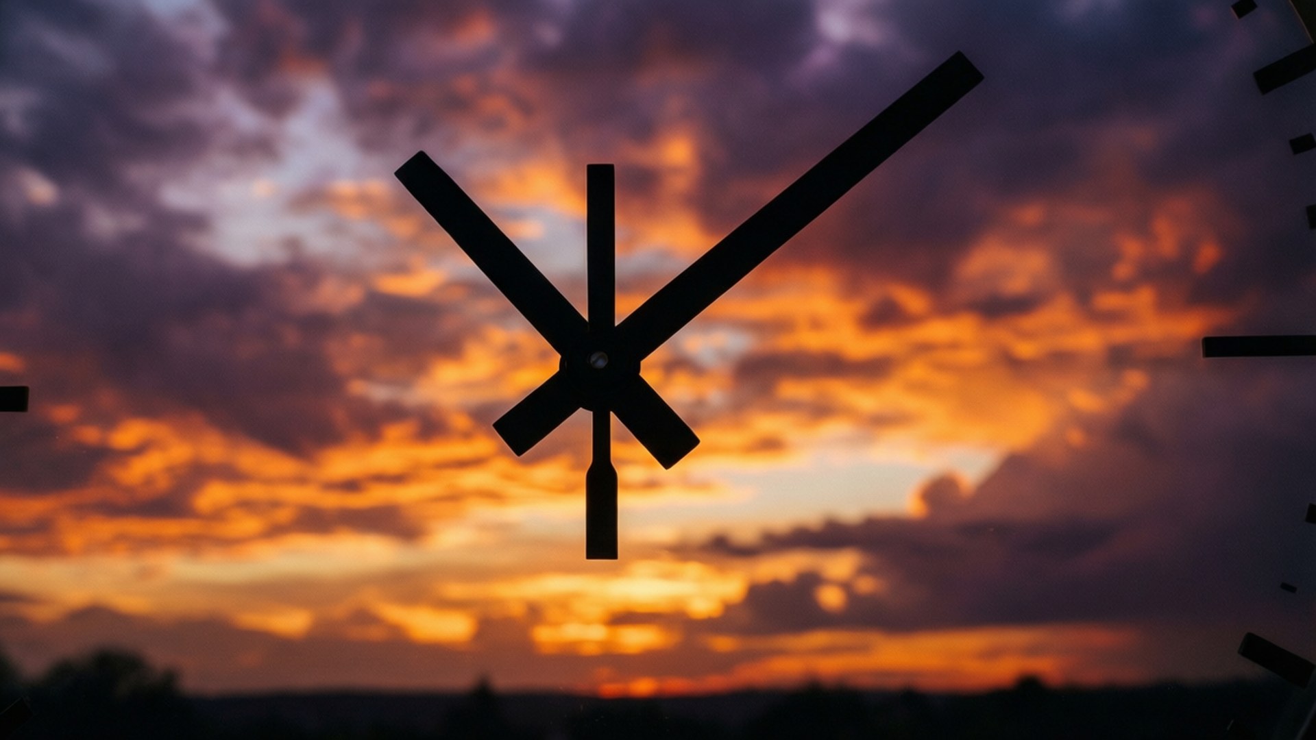 Sunset Silhouette Hands 壁紙 — 剪影時鐘指針框住一個戲劇性的日落天空，燃燒著橙色、紫色和金色的雲彩。