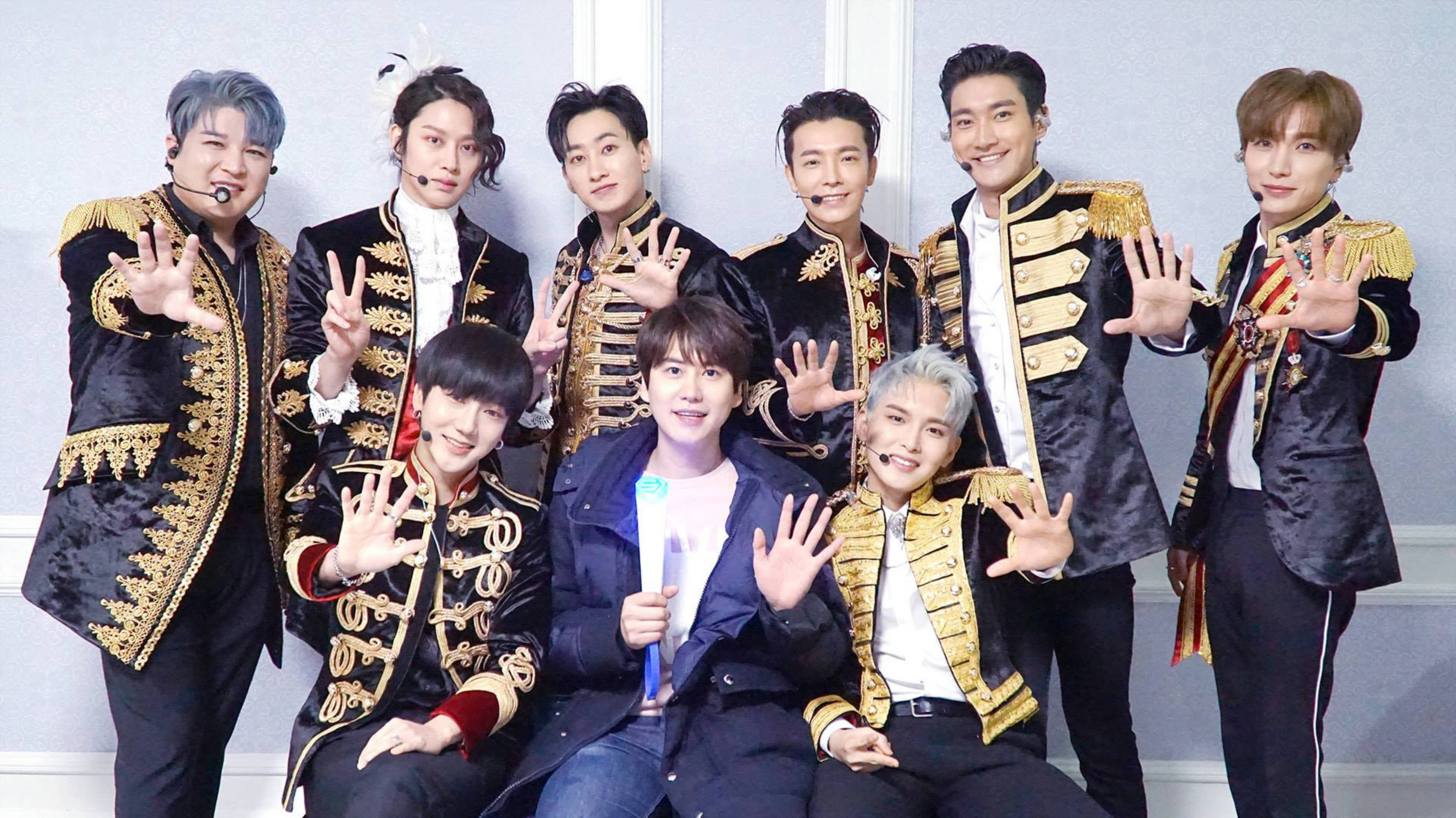 Super Junior 王子服裝造型 壁紙 — 七名身穿華麗黑金軍裝風格外套的男子，在樸素的淺藍色牆壁前愉快地擺姿勢。