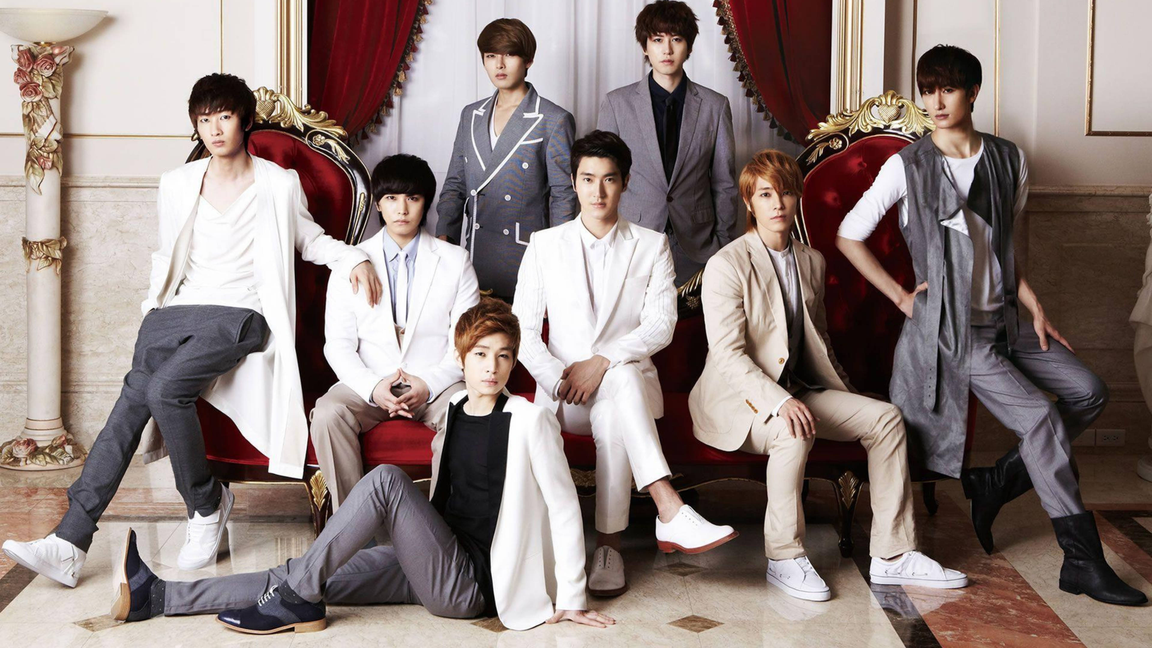 Super Junior 王者風采 壁紙 — 七位時尚年輕男士身穿白色和灰色西裝，在豪華鍍金房間的華麗紅色椅子上自信地擺姿勢。