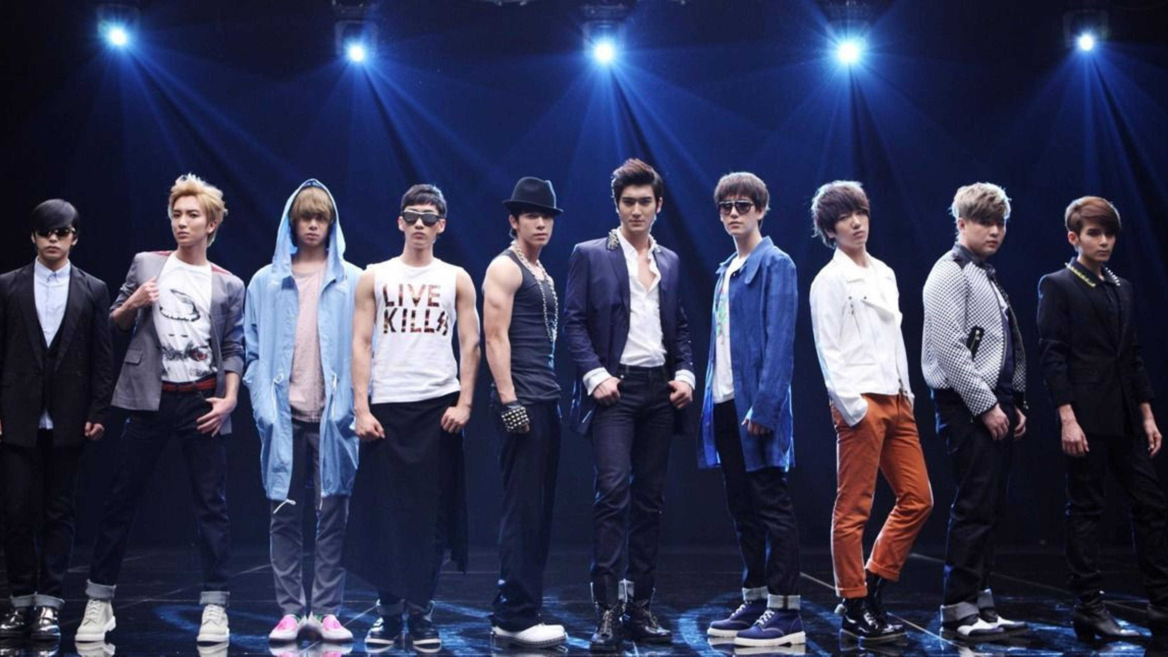 Super Junior 舞台照 壁紙 — 一個K-pop男團自信地站在黑暗的舞台上，被明亮的藍色聚光燈照射，帶有戲劇性的光束。