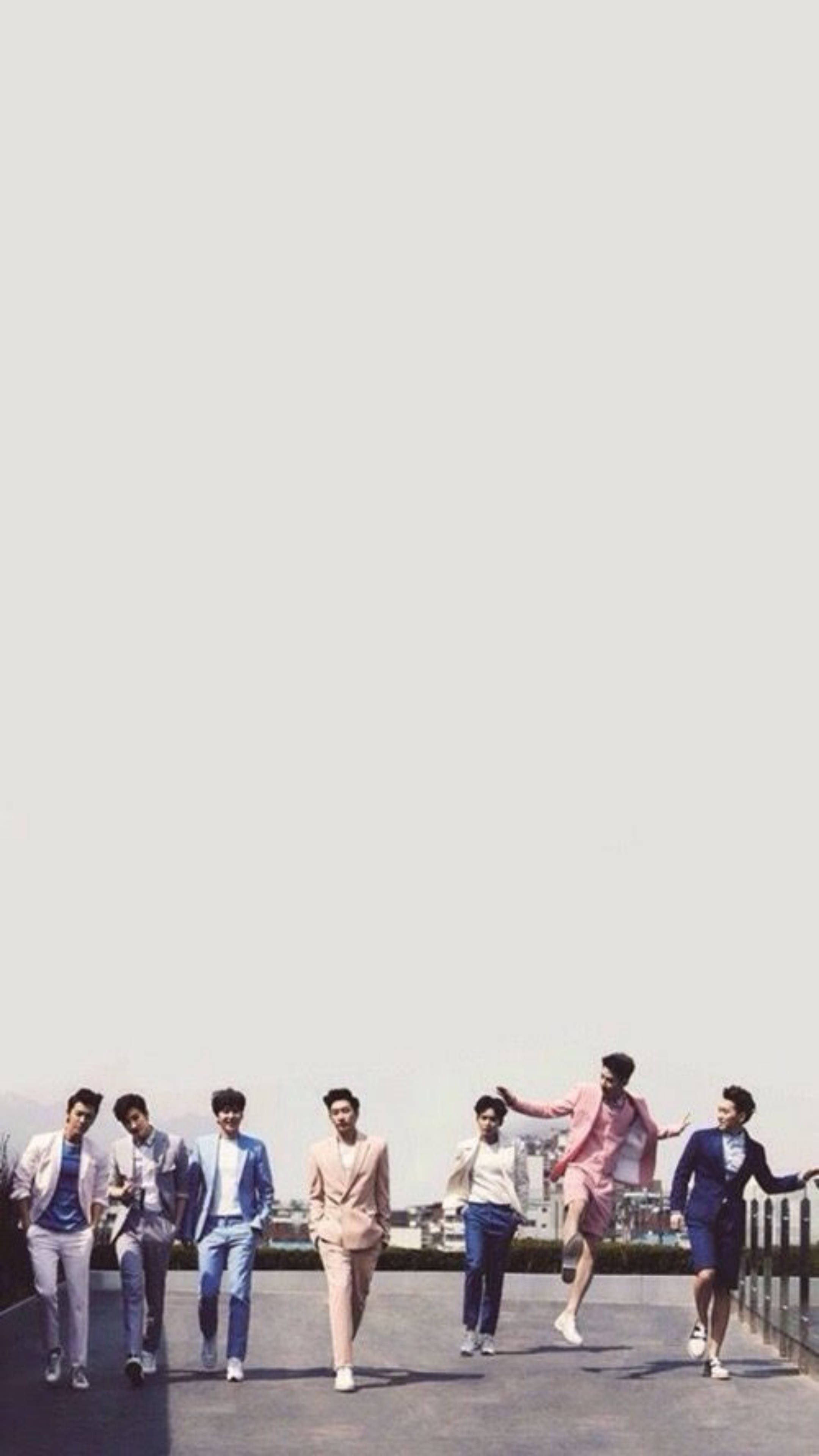 Super Junior 街頭照 壁紙 — 七位穿著粉彩色西裝的時尚男士，在朦朧的城市天際線背景下，於屋頂上歡快地大步走和跳躍。