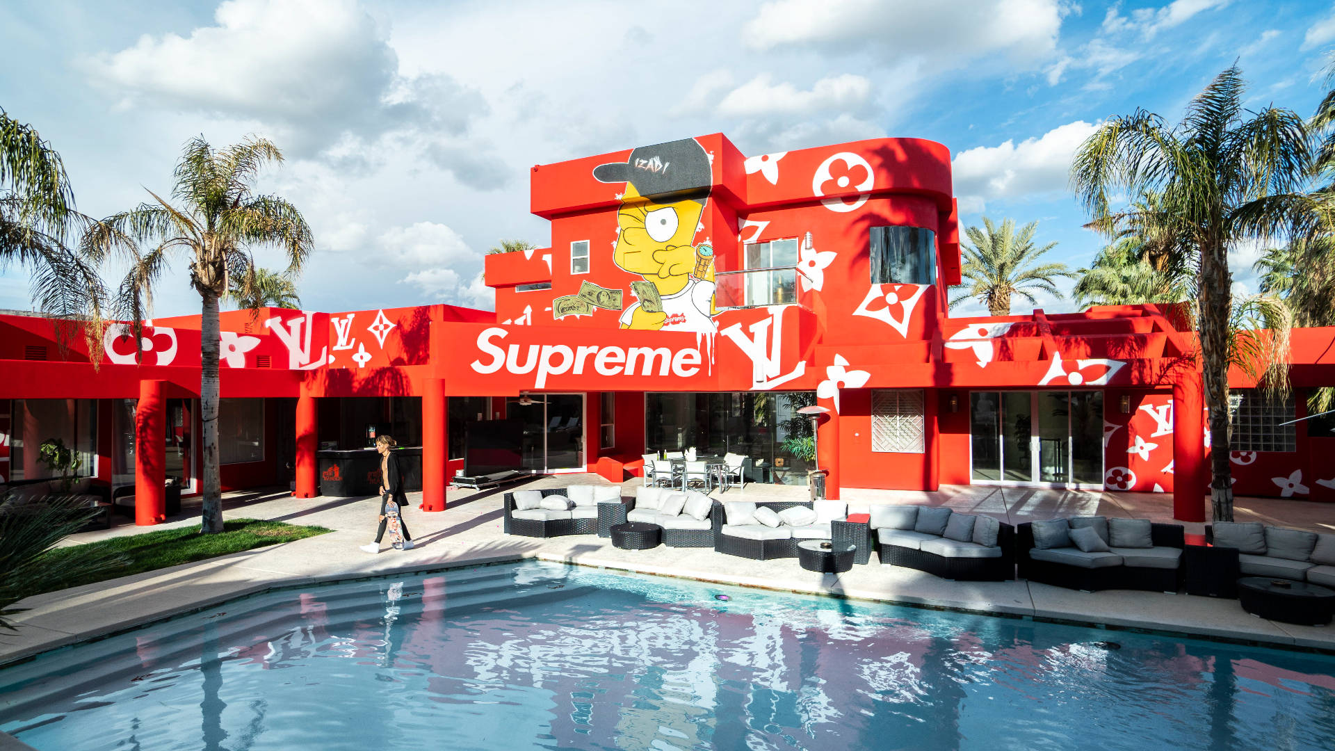 巴特豪宅 Supreme 筆記本電腦壁紙 壁紙 — 一座大膽的紅色建築，帶有巨大的辛普森壁畫和Supreme品牌，矗立在游泳池旁，棕櫚樹下有躺椅。
