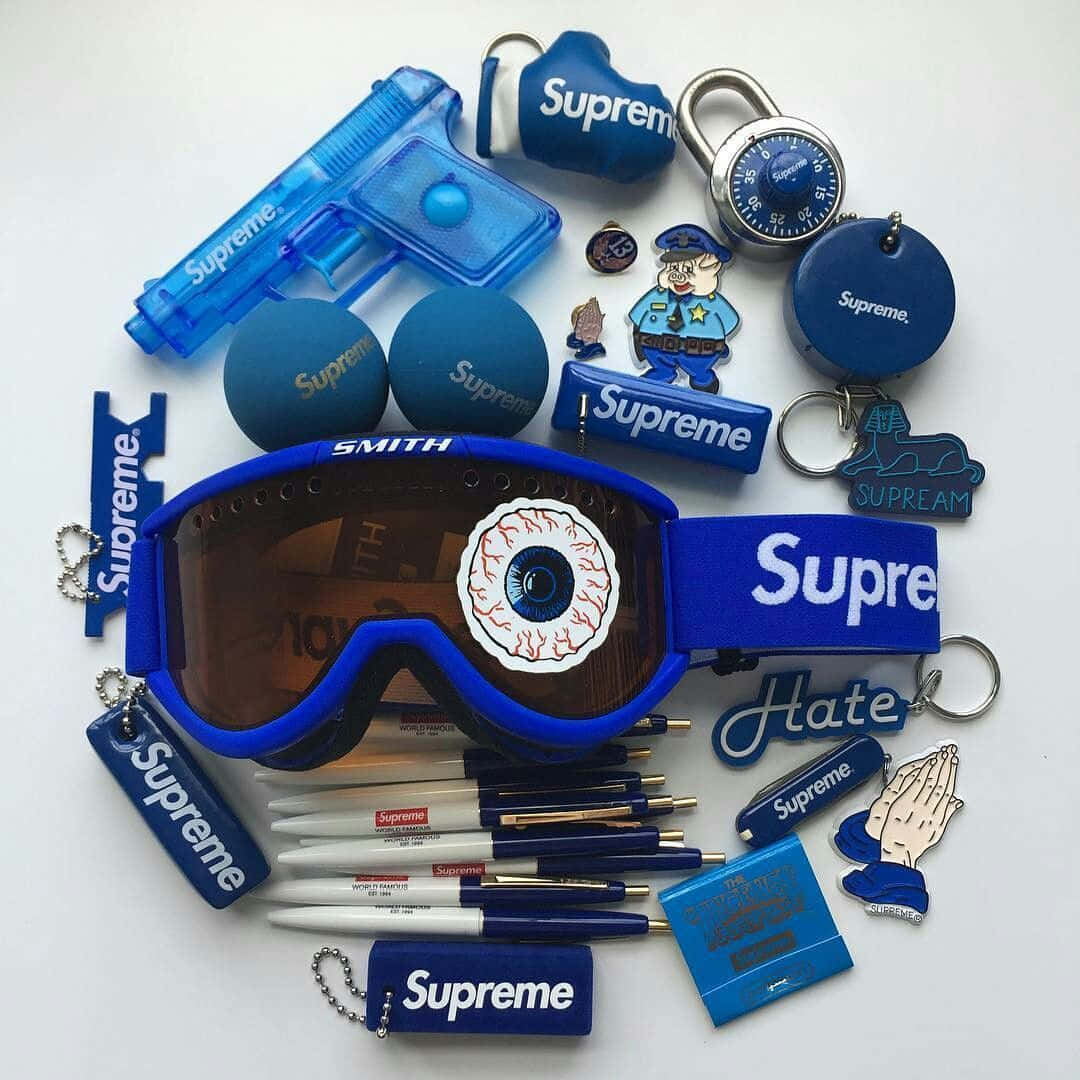 Supreme 藍色系列：奢華時尚的巔峰之作 壁紙 — 白色背景上藍色Supreme品牌商品的平鋪擺放，包括帶有眼睛設計的護目鏡、筆、鑰匙圈和玩具槍。